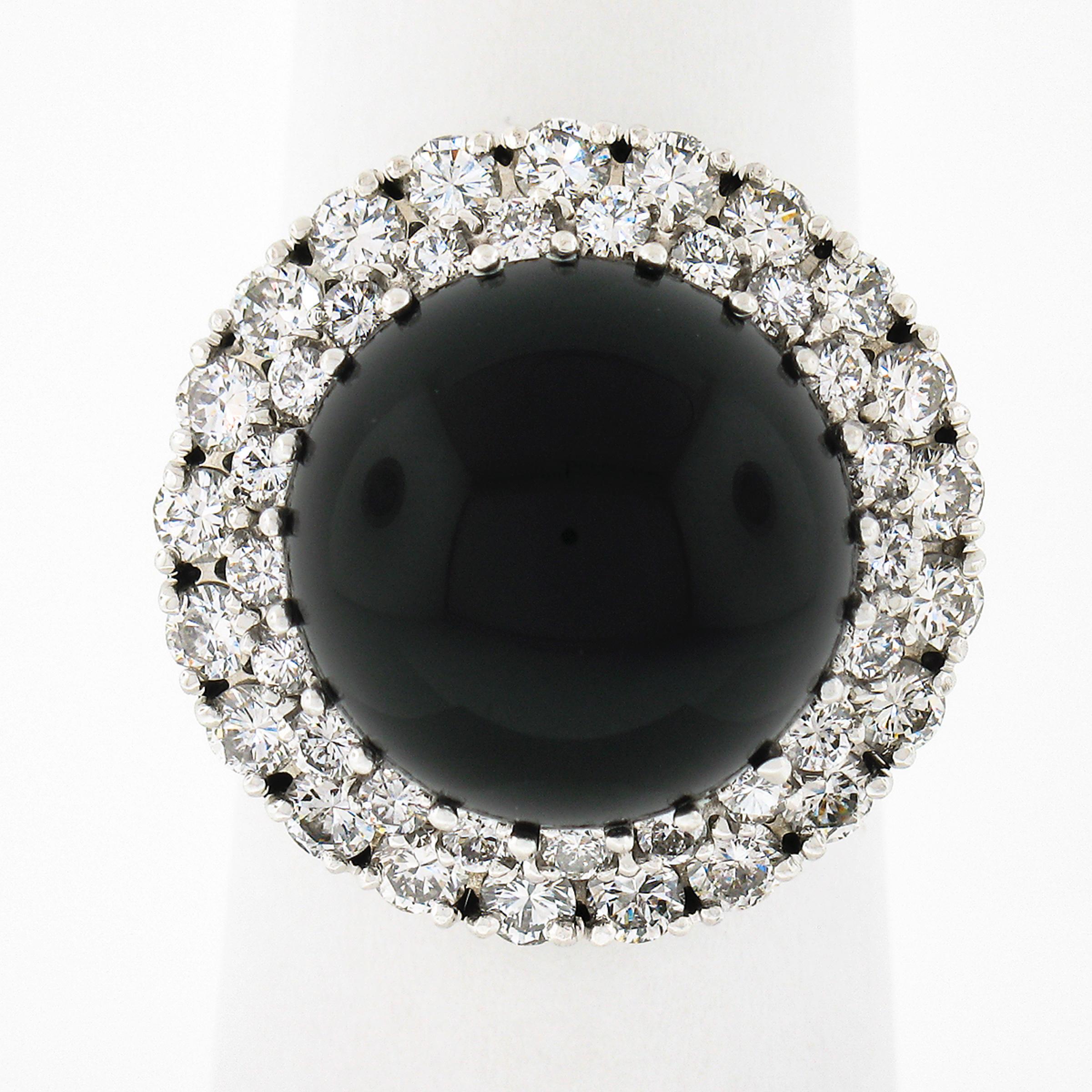 This magnificent vintage cocktail ring is crafted in solid 18k white gold and features a large black onyx solitaire with very fine diamond accents throughout. The bold round cabochon cut onyx shows a nice black color with a polished finish and is