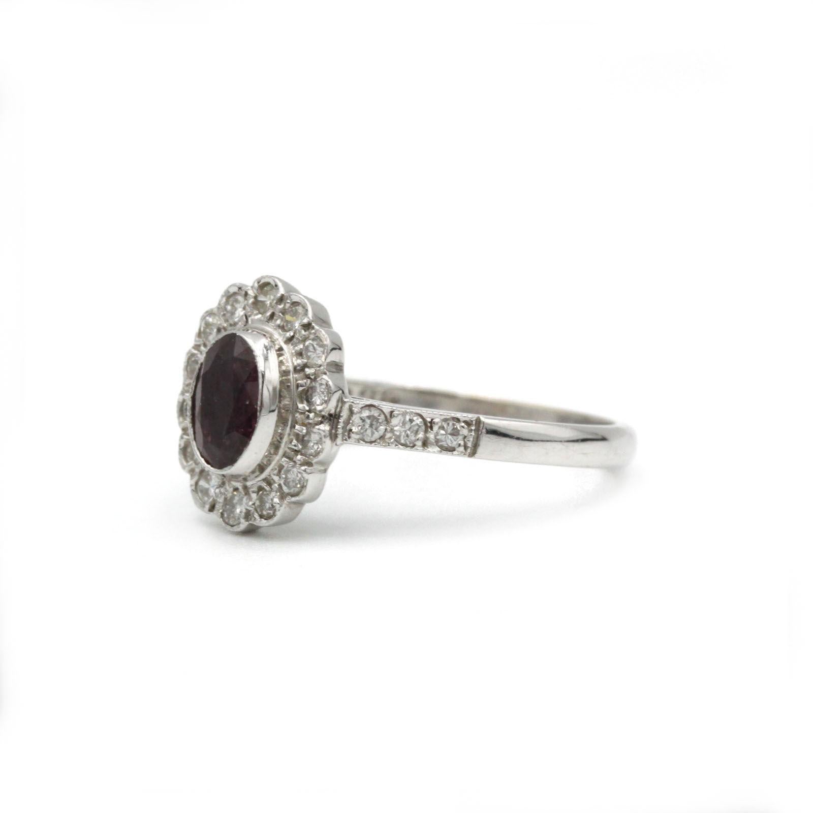 Dieser elegante Vintage-Margeritenring ist ein zeitloser Ausdruck von Anmut und Raffinesse. Er ist aus 18 Karat Weißgold gefertigt und zeigt einen tief purpurroten, ovalen Rubin, der von einem funkelnden Halo aus Diamanten im Brillantschliff
