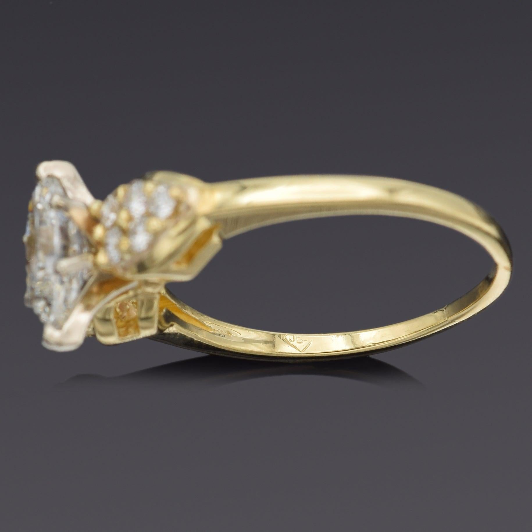 Un refinado anillo de compromiso elaborado en oro amarillo de 18 quilates, con un diamante de talla ovalada en el centro. El diamante está acentuado por grupos de diamantes brillantes redondos a cada lado en forma de pera, que realzan su brillo y le