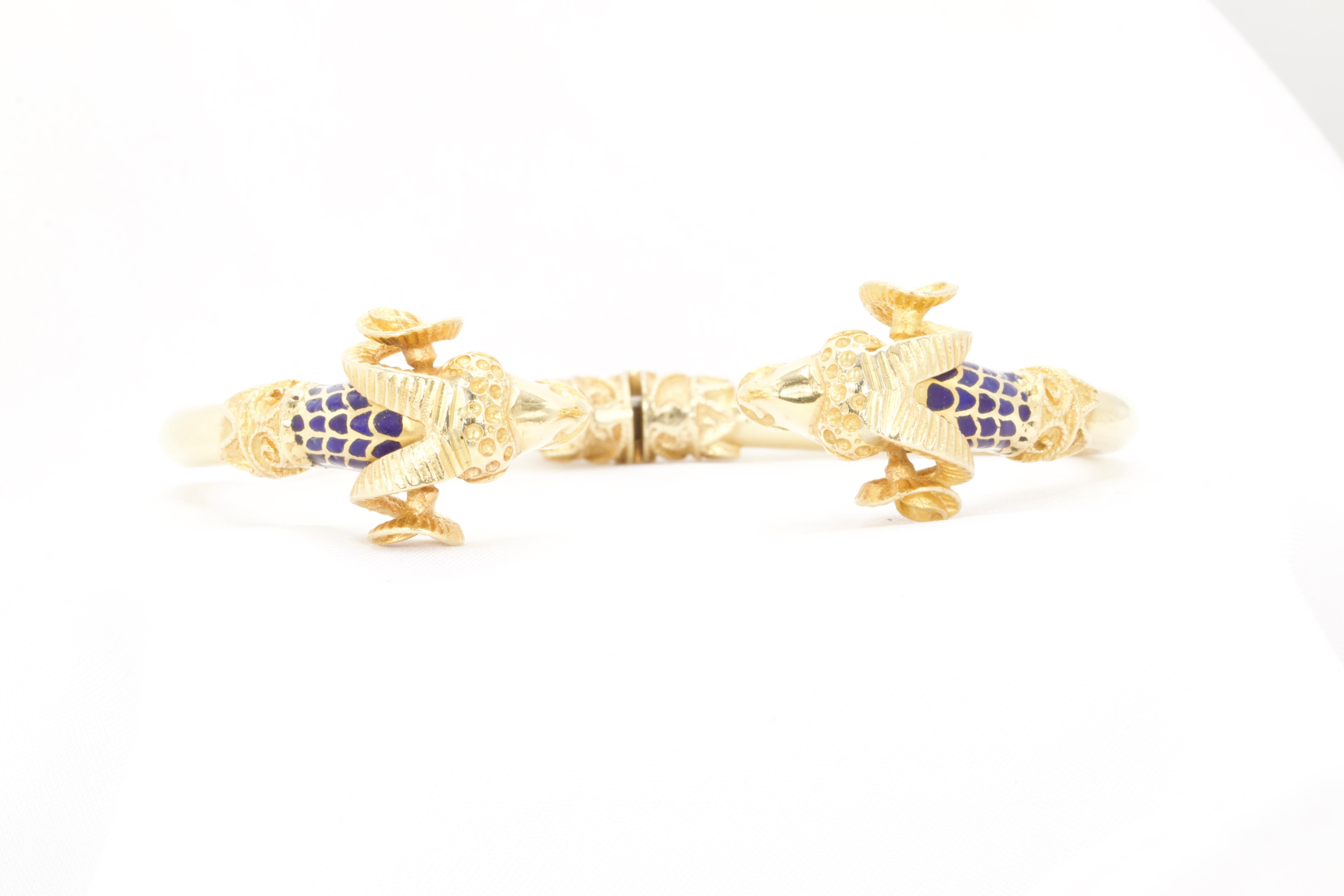 Ce bracelet à charnière vintage, datant des années 1980, respire l'élégance intemporelle. Méticuleusement réalisé en or jaune 18 carats, il présente un remarquable motif à double tête de bélier rehaussé d'émail bleu. D'une largeur de 4,8 mm et d'un