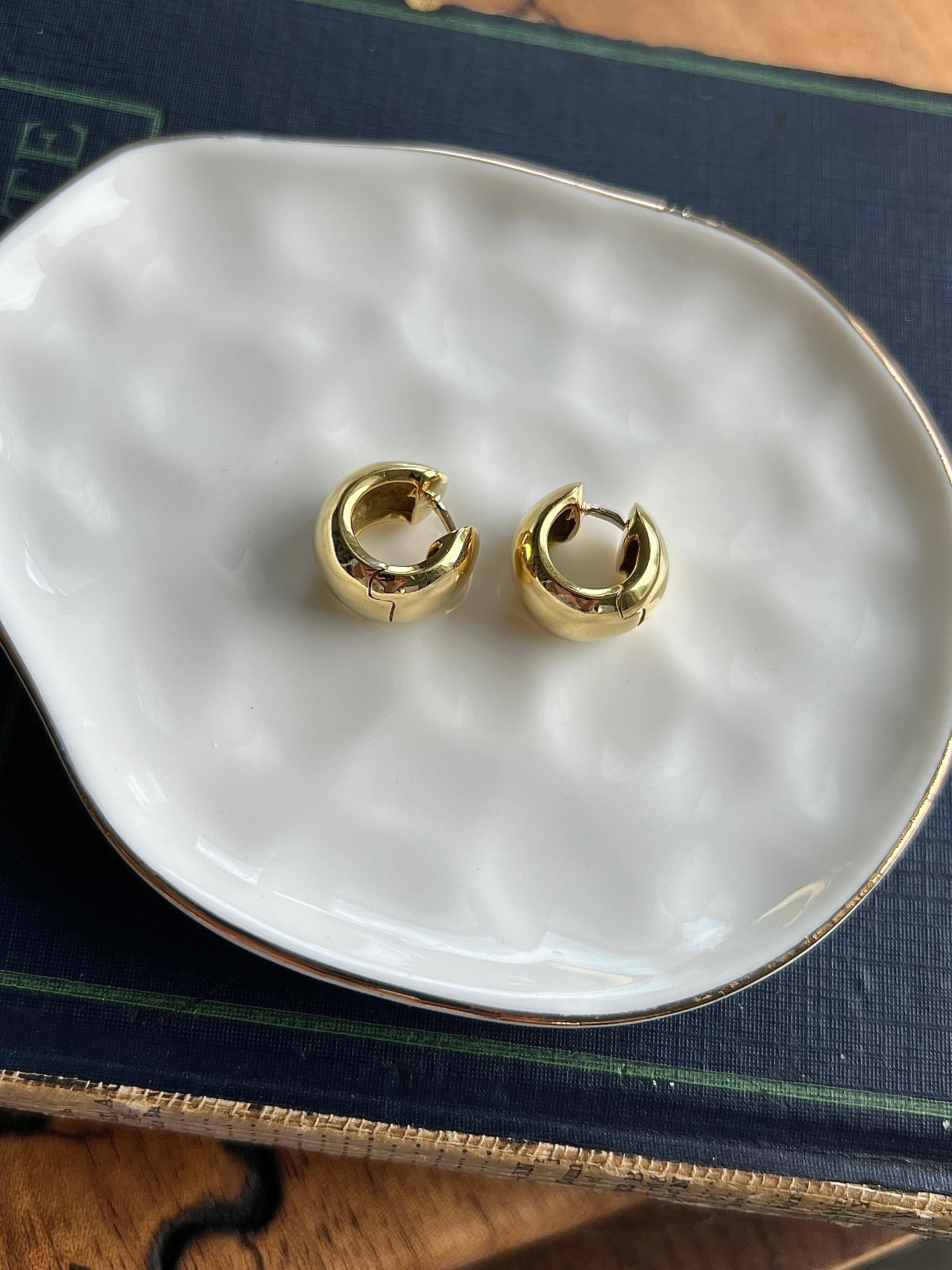 This pair of vintage 18 karat yellow gold chunky huggie hoop earrings offers timeless style with a bold, minimalist edge. Crafted in a classic circular silhouette, the hoops feature a rich, high-polished finish that highlights the warm luster of the