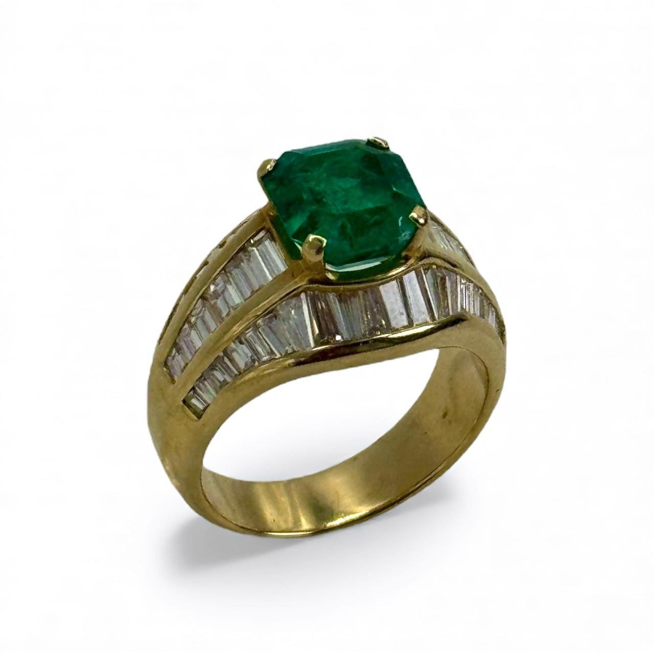 Un sorprendente anello vintage realizzato in oro giallo 18 carati, con al centro uno squisito smeraldo naturale da 2,57 carati dal colore verde intenso e vivido. Lo smeraldo è affiancato da diamanti taglio baguette meticolosamente incastonati a