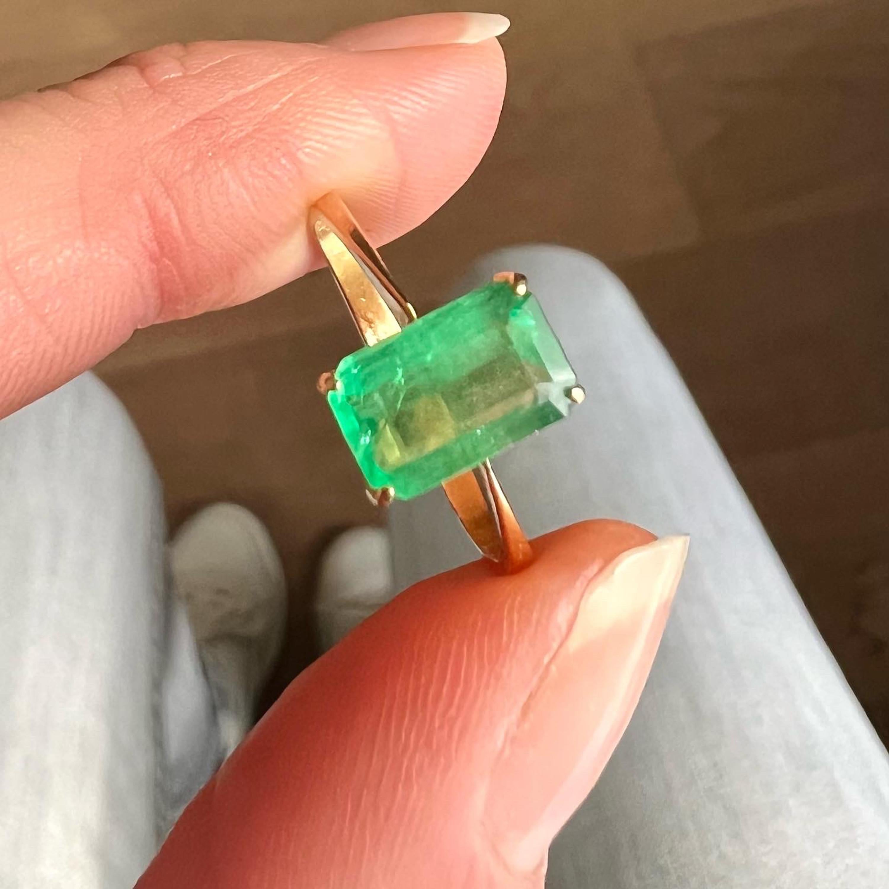 A gorgeous yellow gold vintage emerald cut emerald ring. The natural emerald gemstone has a rich vibrant color and is set in a classic gold band rendered in 18 karat yellow gold. The step cut faceted rectangle green emerald sits along with four soft