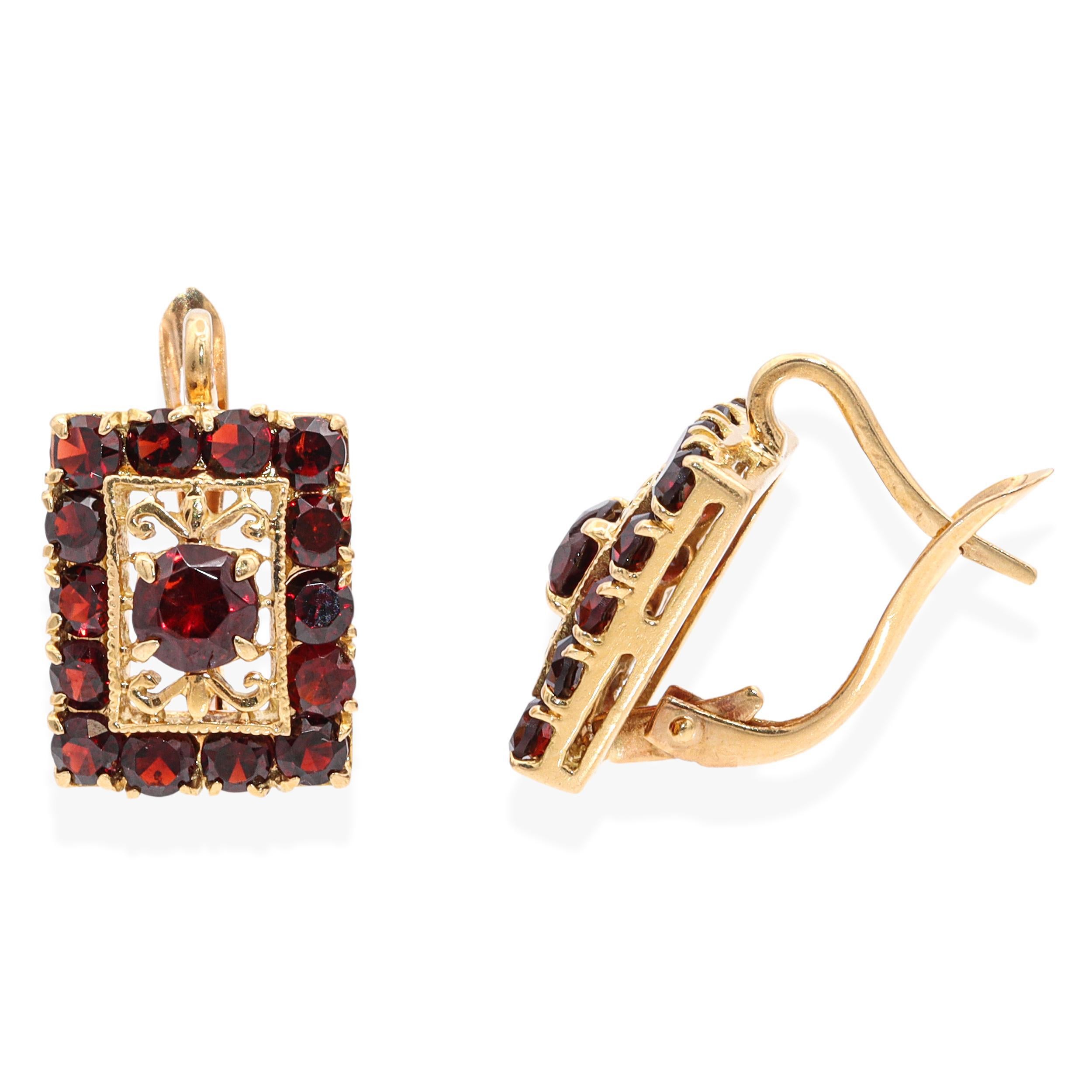 These exquisite antique earrings are crafted in rich 18K yellow gold and set with deep red garnets that exude timeless elegance. Each earring features a rectangular design, centering a round-cut garnet framed by ornate filigree scrollwork.