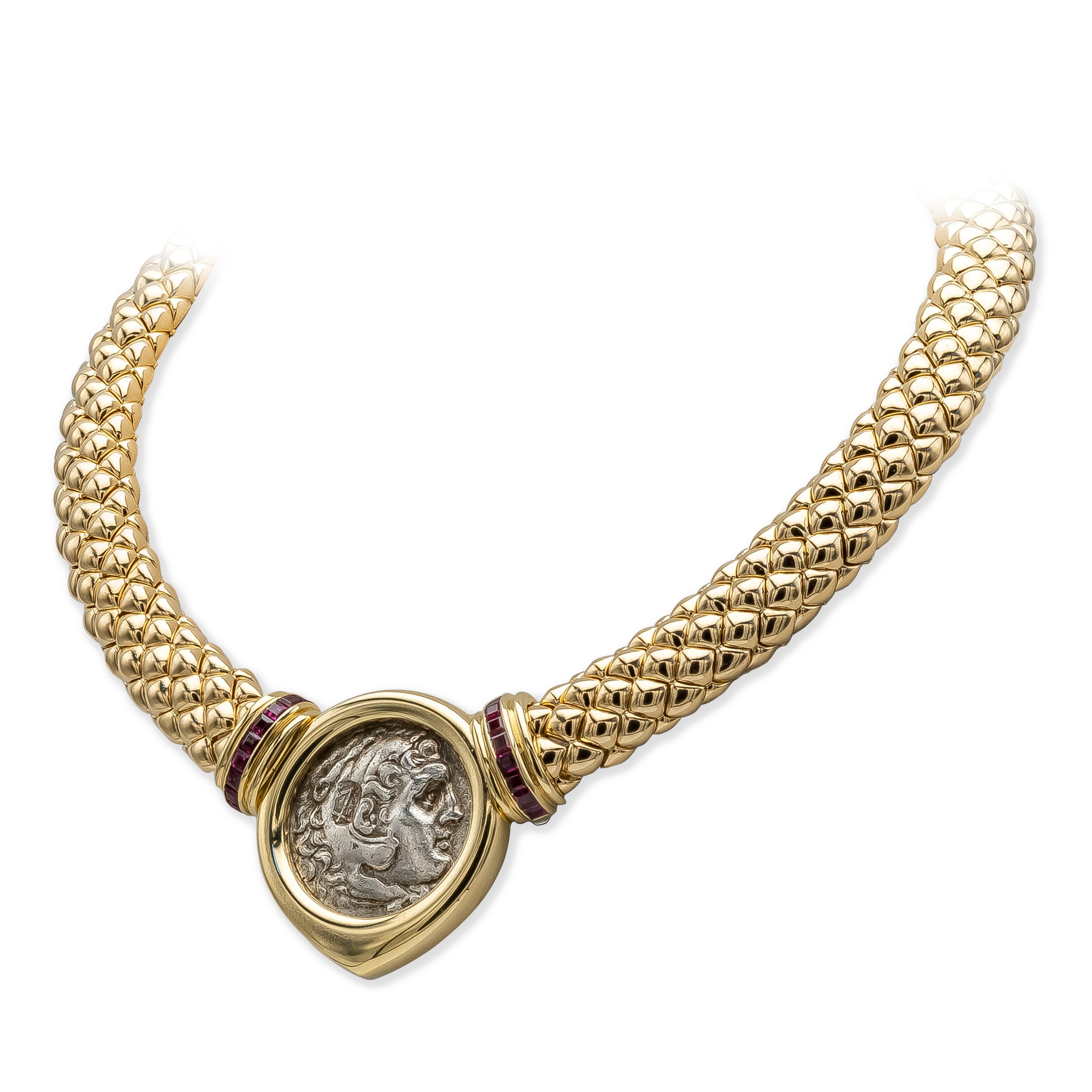A thick collar necklace, featuring a snake skin design made with solid 18K yellow gold and a removable Greek silver drachma coin of Alexander the Great. Accented by a row on each side of princess cut rubies weighing 2.70 carats total and designed