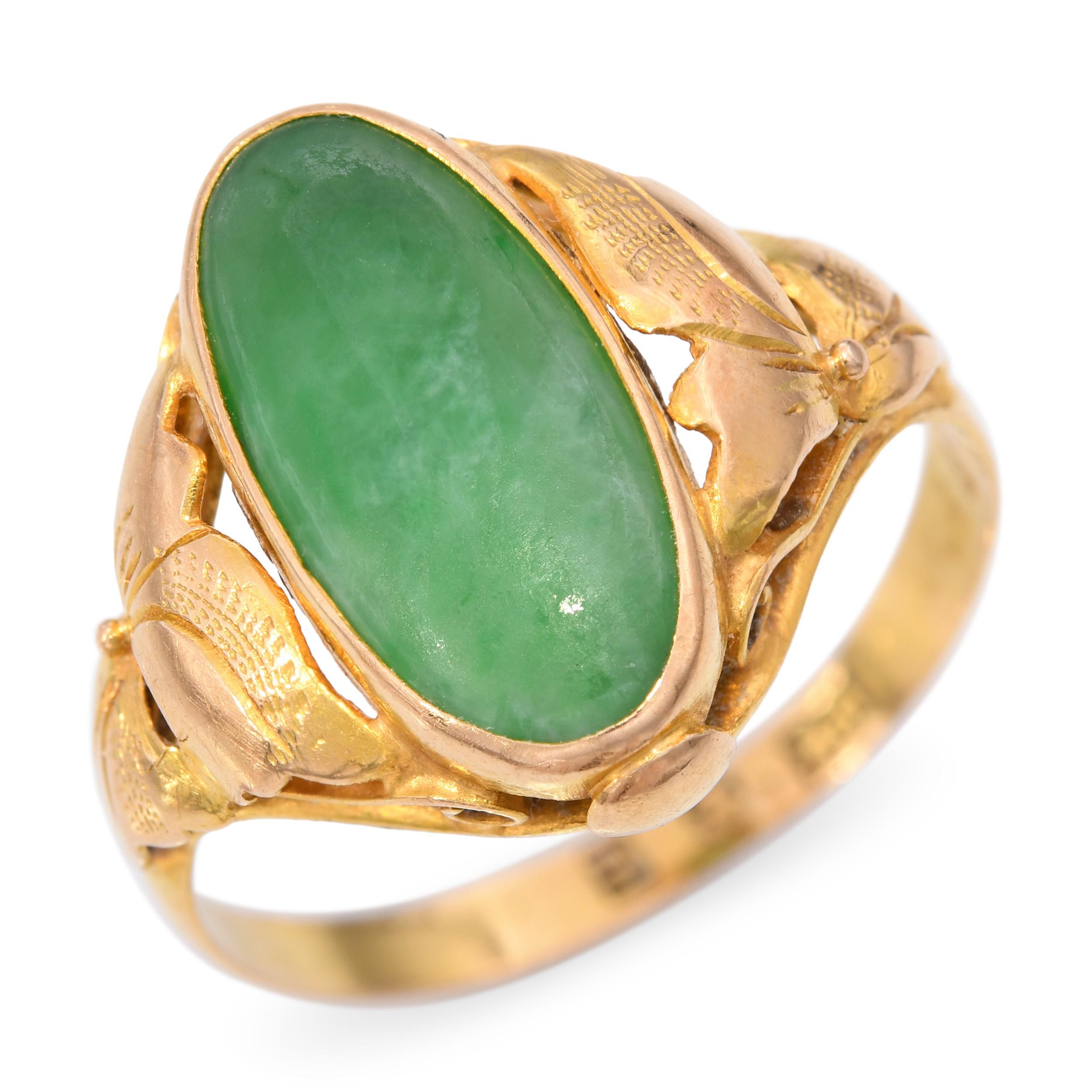 This vintage 18k yellow gold ring features a carved jade centerpiece complemented by a delicate floral motif, combining natural beauty with elegant design. The jade’s smooth polish and subtle green hue are enhanced by the warm gold setting, creating