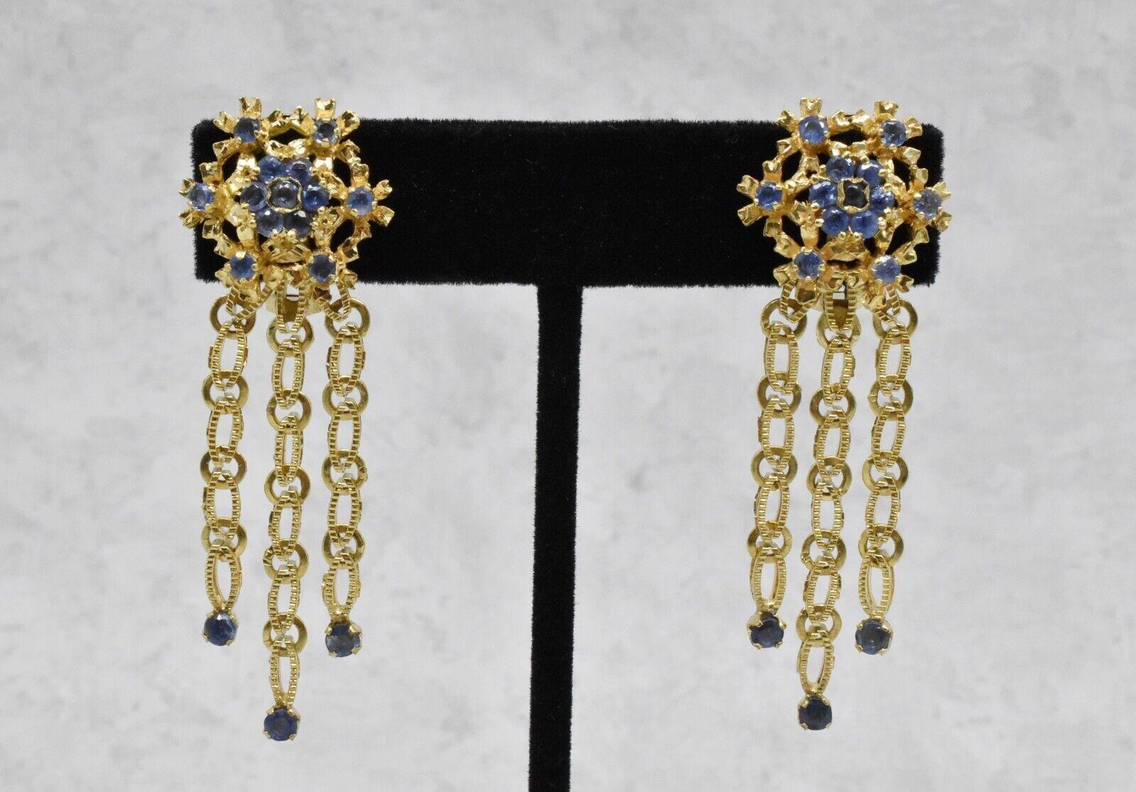 Dieses exquisite Vintage-Schmuckset besteht aus einem passenden Armband und Ohrringen aus 18 Karat Gelbgold, die mit blauen Saphiren verziert sind. Das Armband besteht aus mehreren Reihen strukturierter, ovaler Glieder, die in einer verzierten, mit