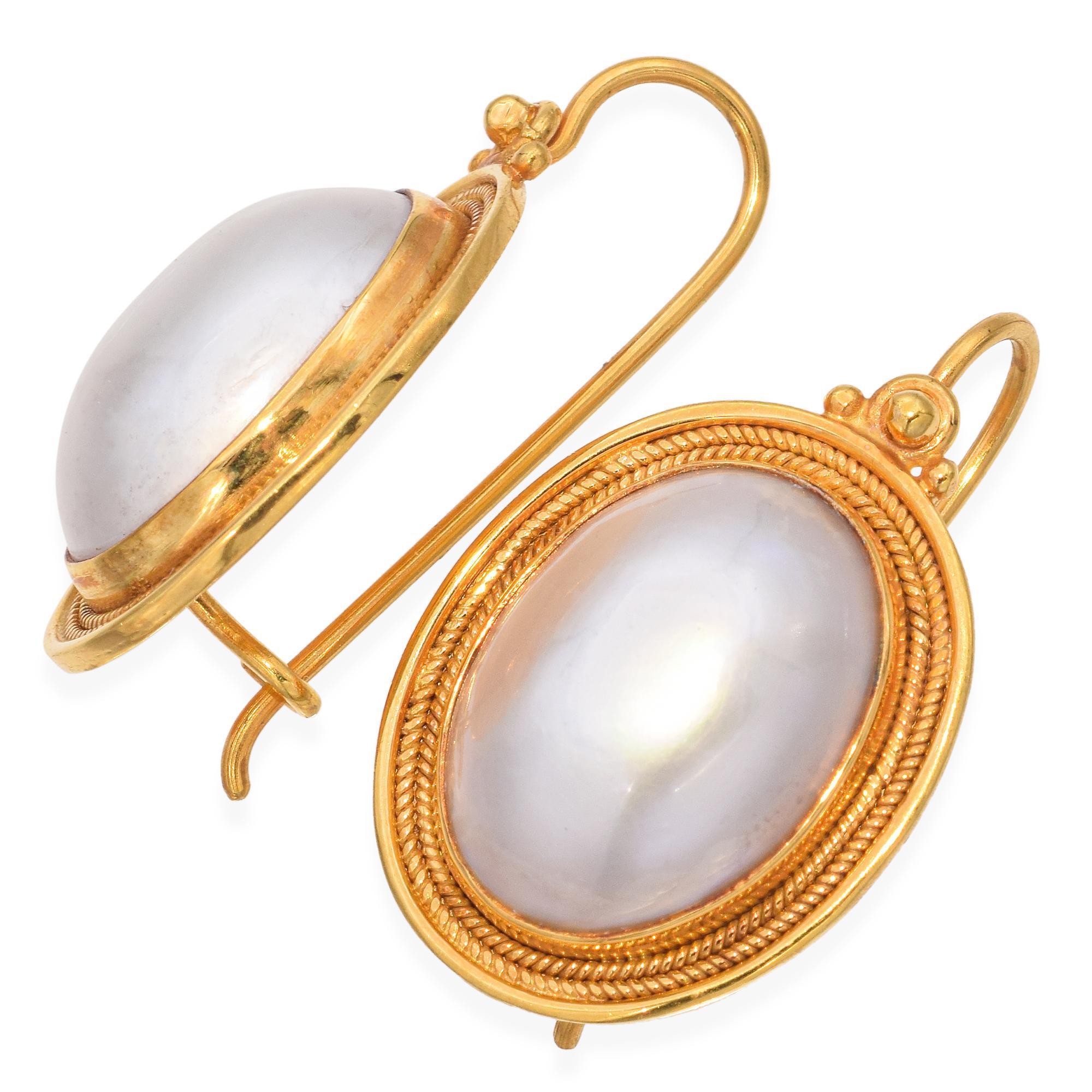 These exquisite earrings are crafted in gold, featuring large oval mabe pearls set in a beautifully detailed gold frame. The frame showcases intricate rope-like detailing around the edge, adding a touch of sophistication. The earrings are designed