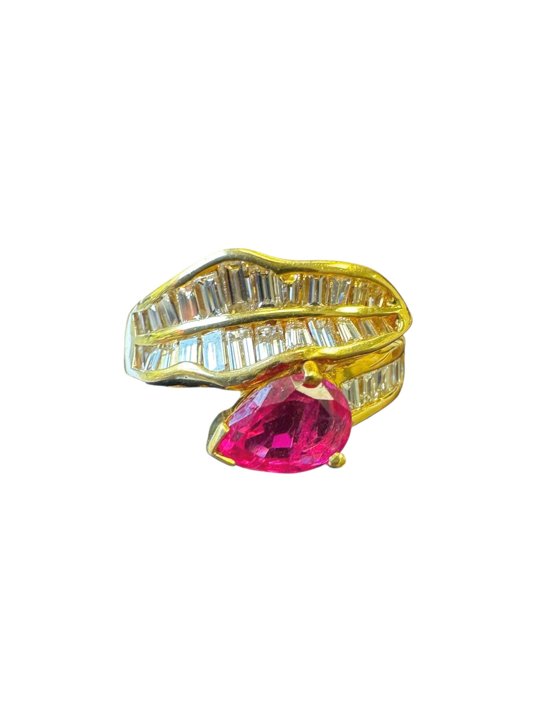 A sculptural and sophisticated vintage swirl ring crafted in rich 18K yellow gold, showcasing a vivid pear-shaped ruby weighing approximately 1.12 carats. The ruby is framed by an elegant bypass swirl design, encrusted with tapered and straight