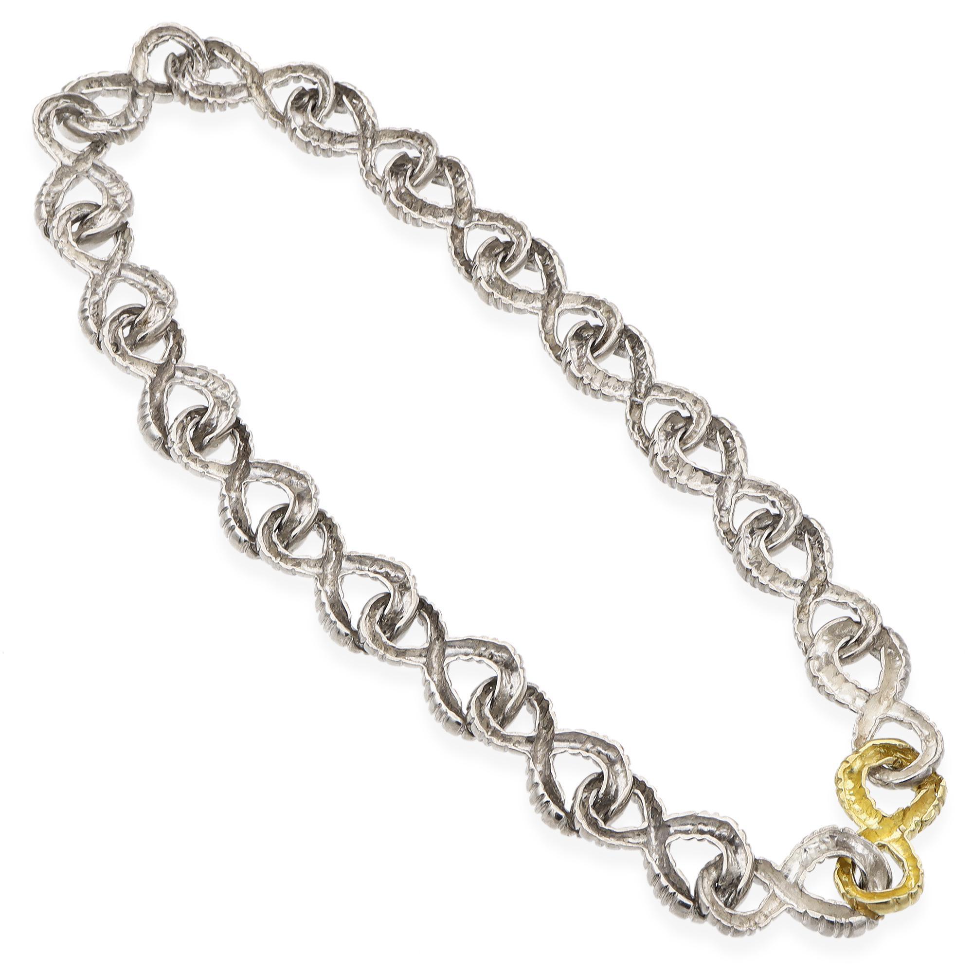 This striking necklace is meticulously crafted in sterling silver. The design features a series of twisted links, creating a continuous loop pattern. A single link is highlighted in 18k gold, adding a touch of contrast and elegance.

Weight: 99.8