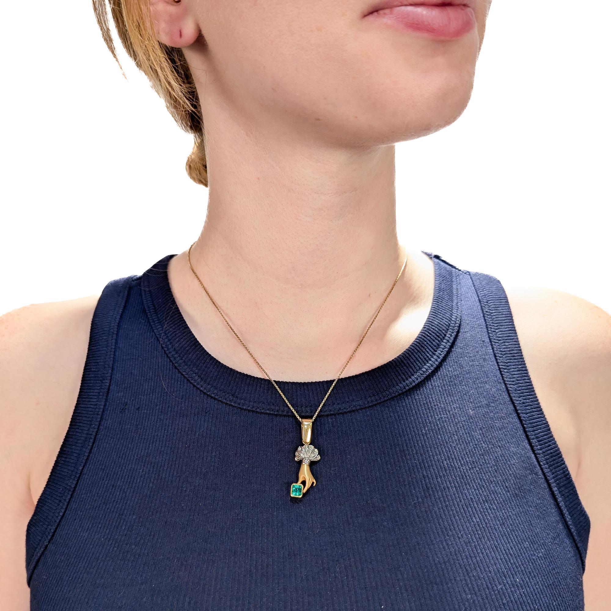 Un raffinato pendente vintage in oro, smeraldi e diamanti.

In oro giallo e bianco a 18 carati.

A forma di mano che tiene tra le dita uno smeraldo incastonato. 

Il polso della mano è in oro bianco e presenta un bracciale con diamanti