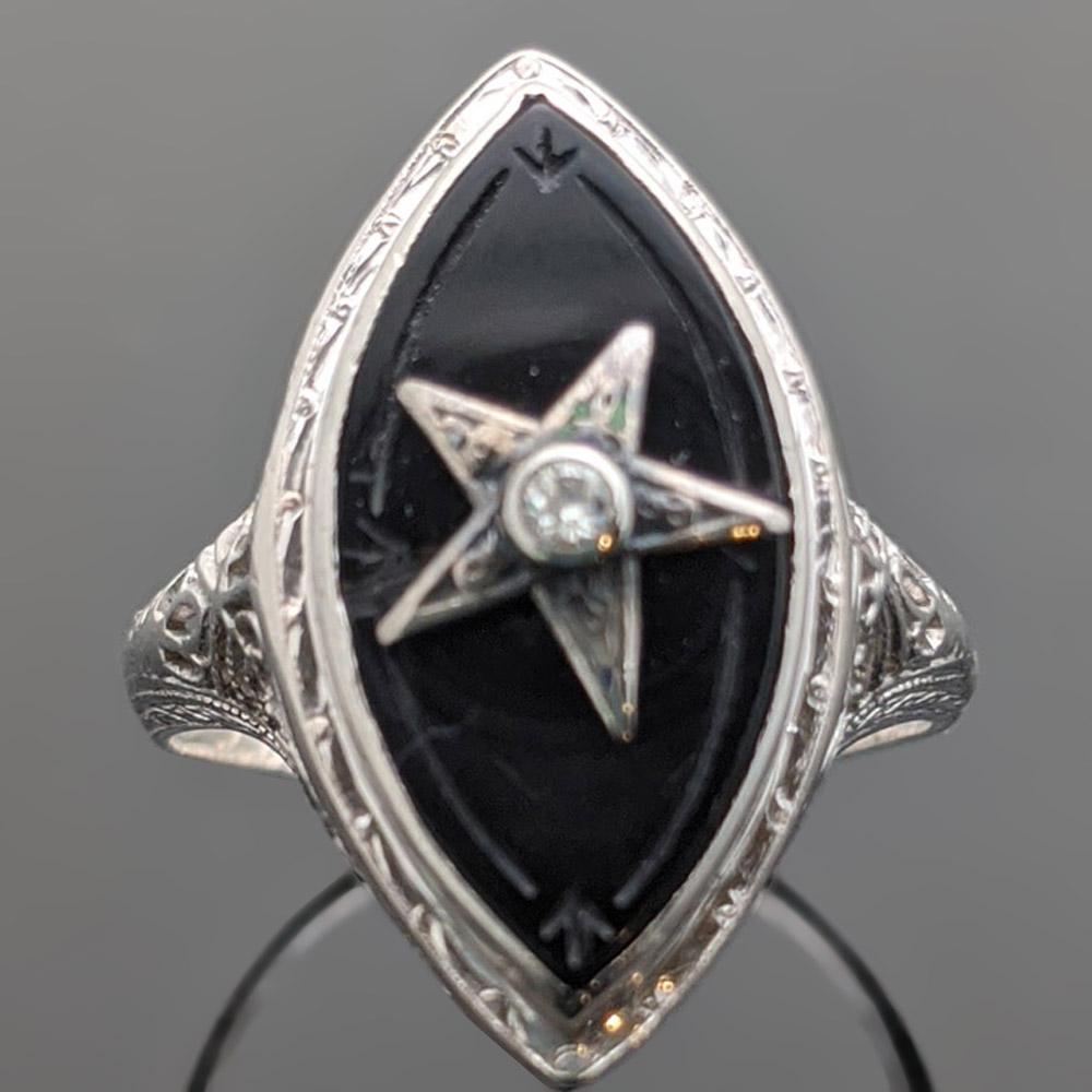This is a vintage 18kt white gold black onyx and diamond ring. Carved black onyx with a white gold star featuring a round brilliant cut center diamond with an estimated weight 0.20 ct. and sculpted setting. Estimated weight of gold 3 gr. 

We will