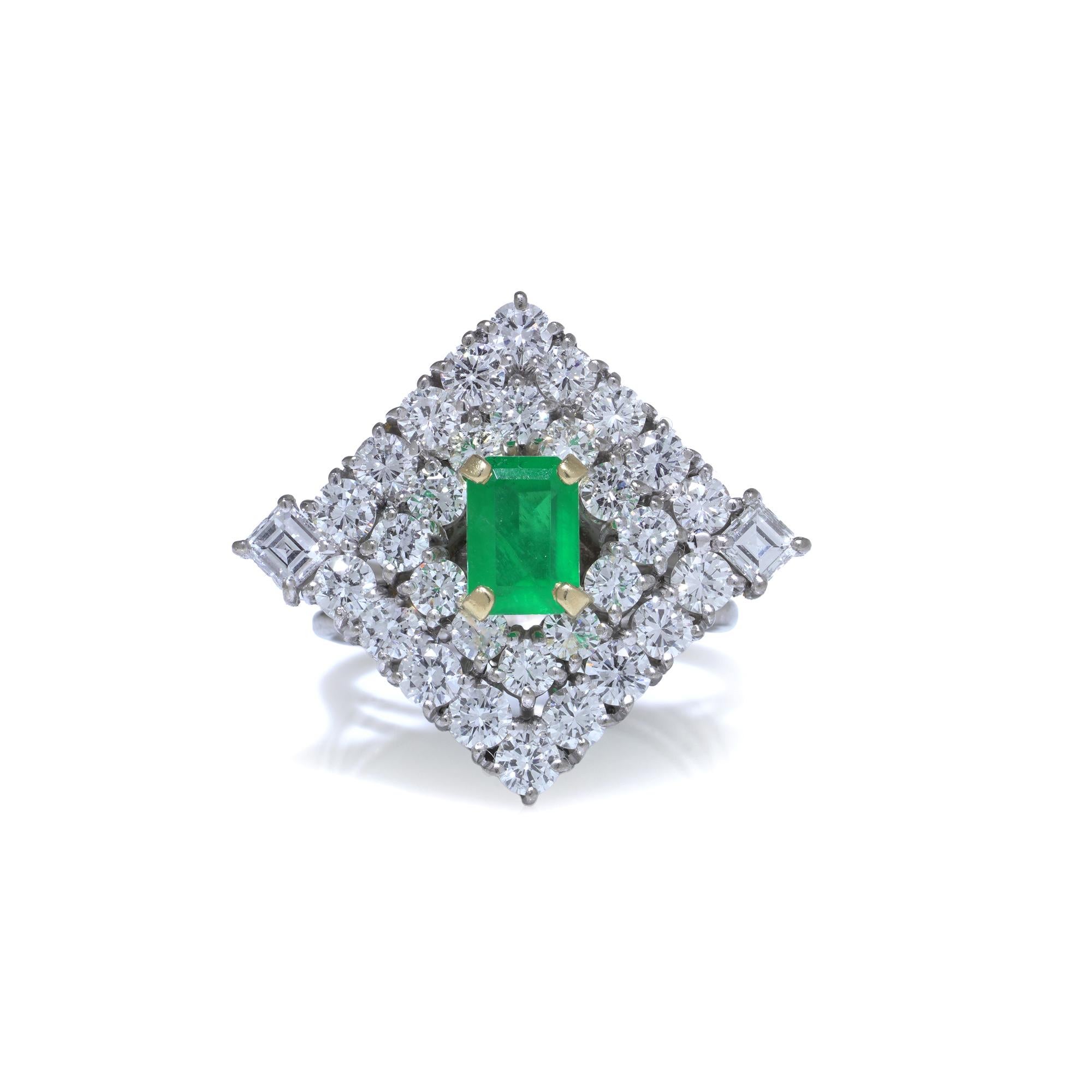 A vintage 18KT white gold emerald ring from the 1970s, designed as a bold emerald cluster ring centred with a natural Colombian emerald. The emerald is an emerald-cut stone of approx. 0.25 ct with minor F2 oil, making it highly desirable for