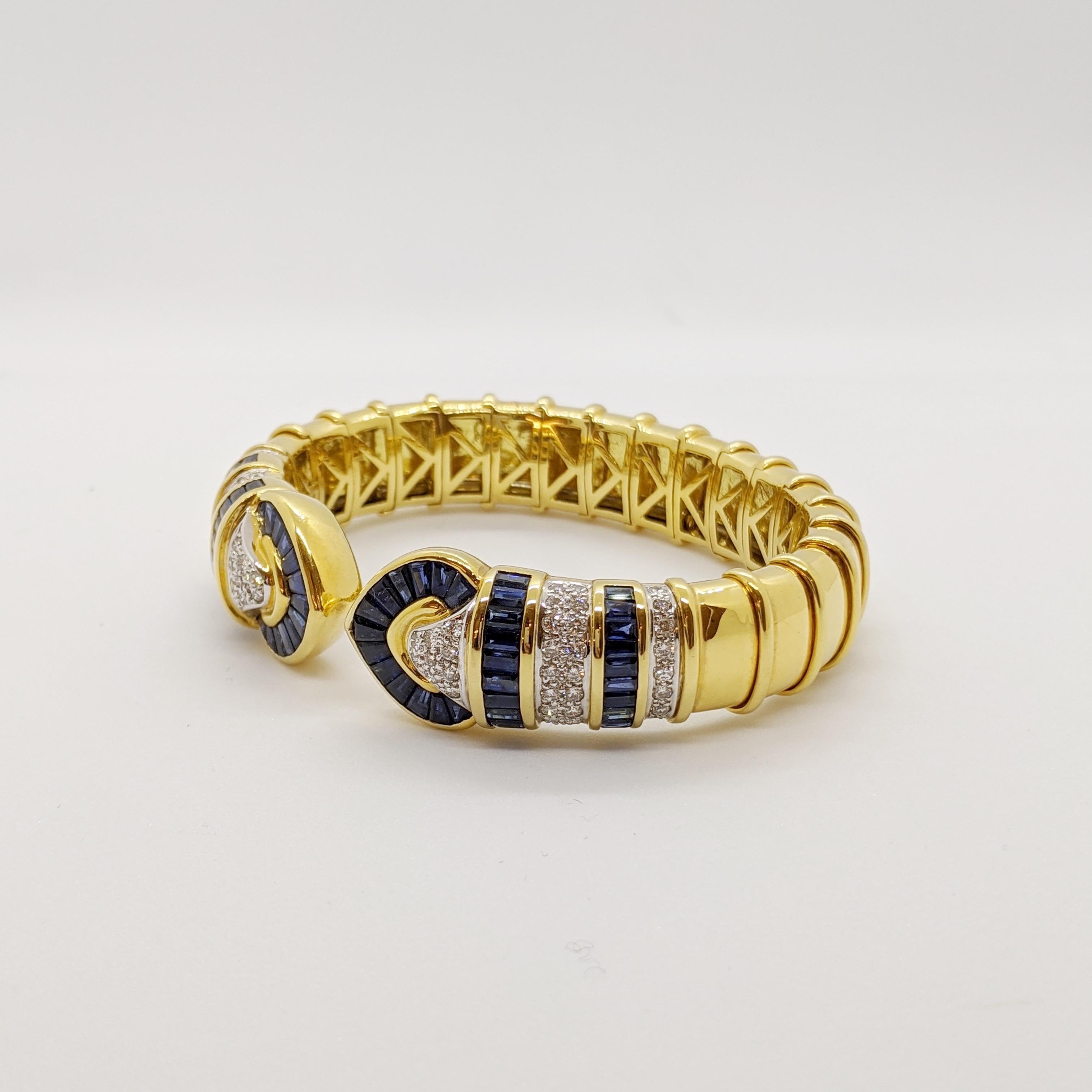 No details were spared in this beautiful 18 karat yellow gold cuff bracelet. Long tapered blue sapphires and pave round brilliant diamonds are set forming two hearts. The design continues with rows of baguette sapphires and pave diamonds. Ribbed