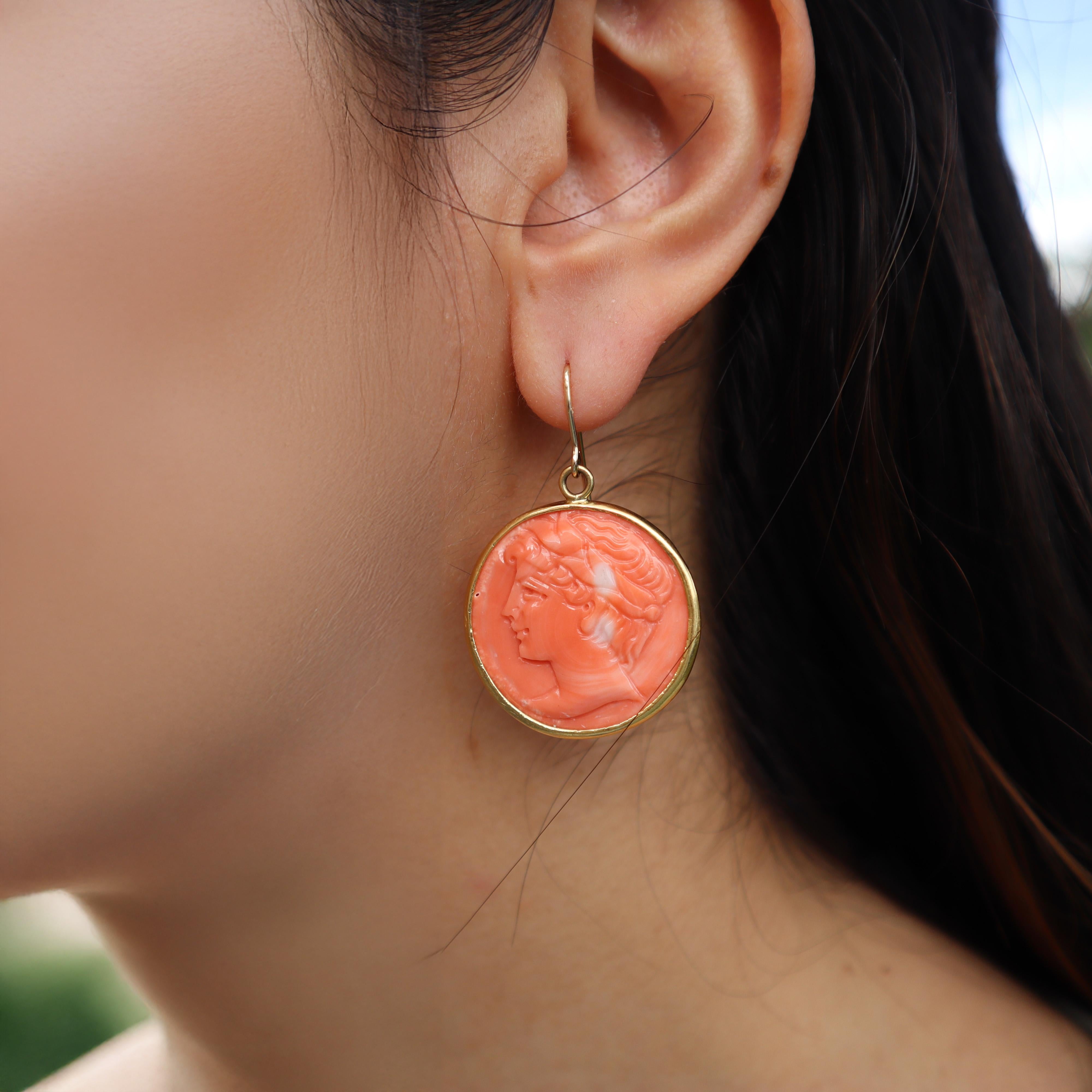 These exquisite vintage 18kt yellow gold earrings are a stunning representation of artistry and history, featuring a prominent piece of coral that beautifully reproduces an ancient Roman coin. 

Each earring showcases intricate engravings that