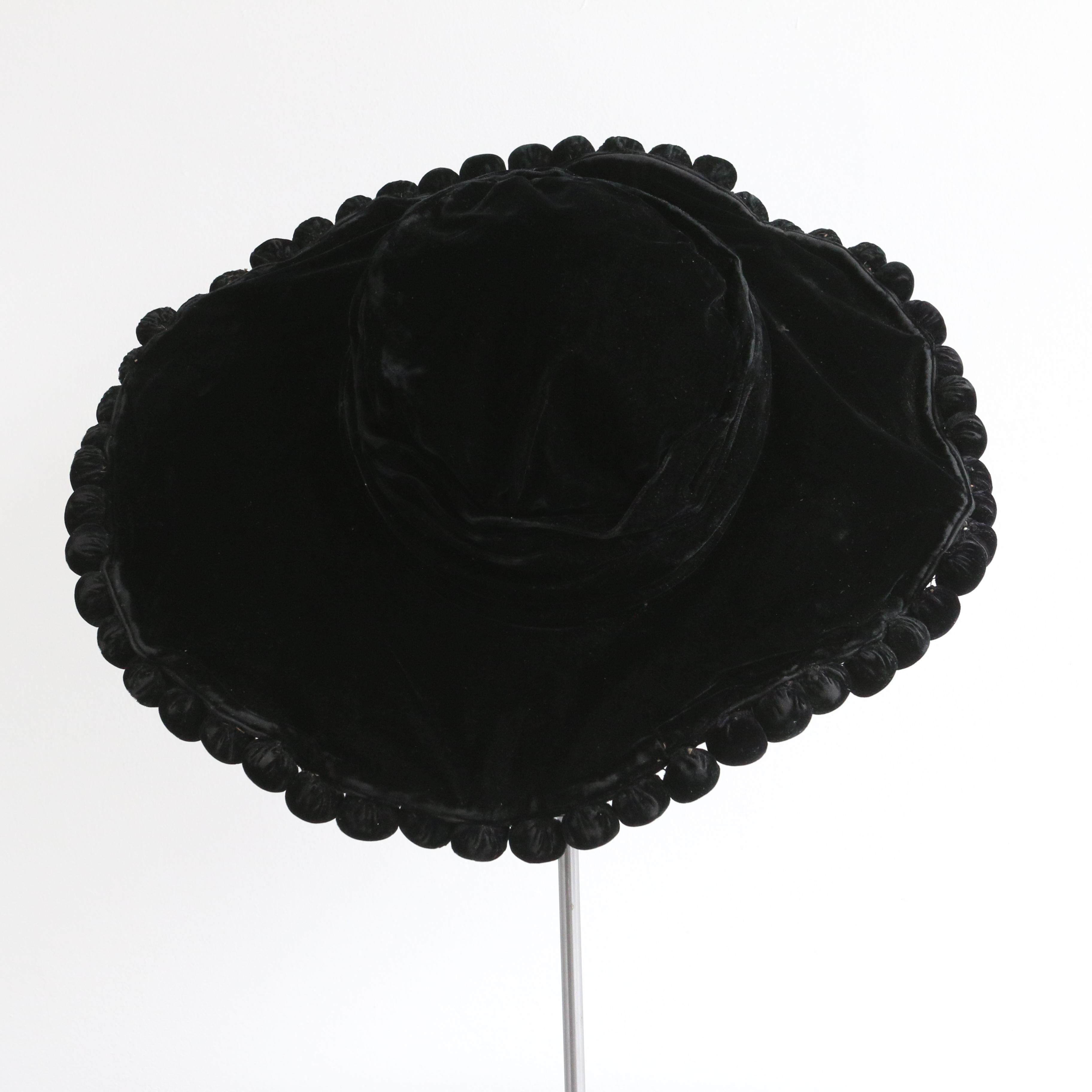 This incredible Edwardian wide brimmed silk velvet hat, with intricate gathered pleats around the crown and a silk velvet pom pom trim around the wired brim, which widens along each side and slims toward the front and back, is the perfect addition