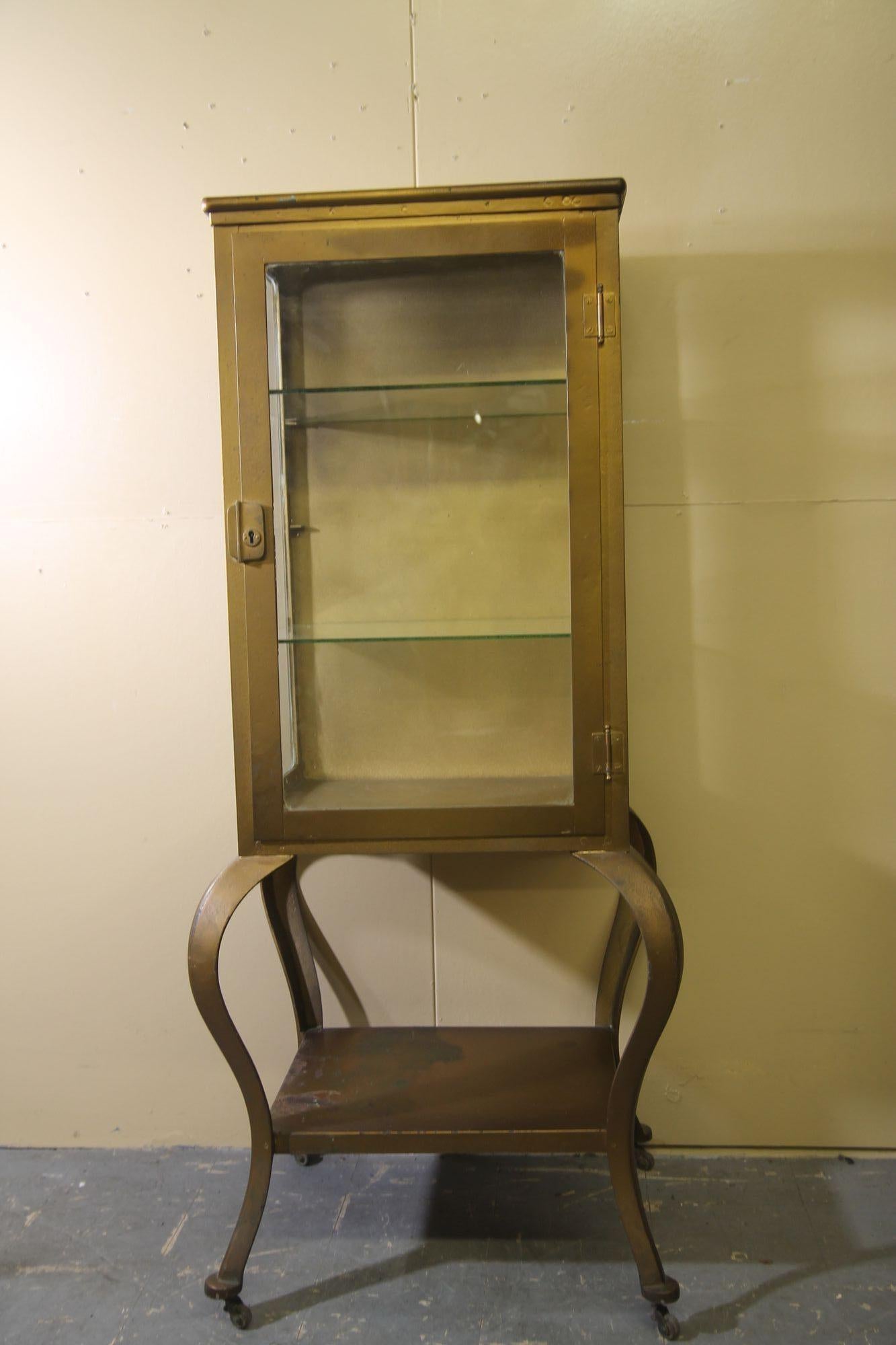 Pleased to offer this great vintage medical cabinet. This cabinet was painted gold many years ago and I think looks great with this finish. This cabinet has a glass door, glass side panels, 2 glass shelves and metal bottom shelf. Im sure you will