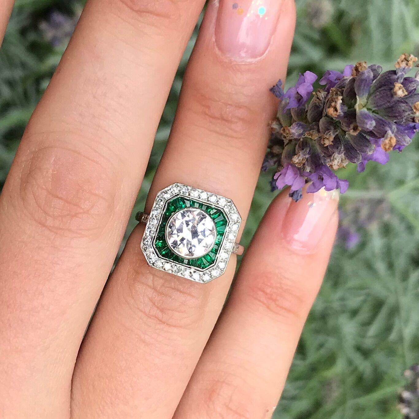 This splendid platinum Art Deco ring radiates straight to your heart; from a 1.55 ct old European cut diamond centre over an octagonal shaped framed set with emeralds and diamonds. As 20 Brazilian emeralds emphasize the impeccable white colour of