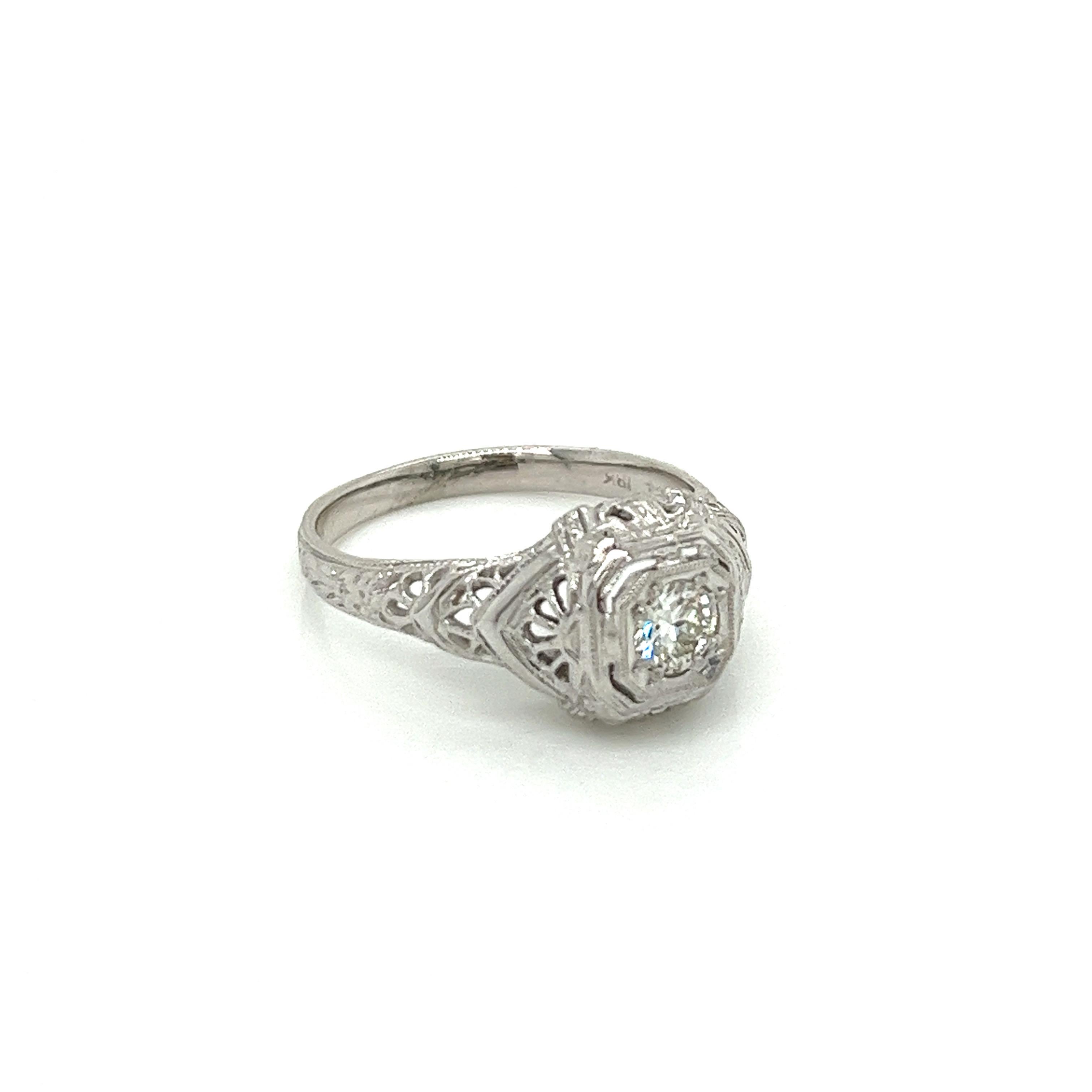 Vintage 1920's 18K White Gold Engagement Ring .22ct. Le diamant central de taille eurpéenne a une couleur H et une pureté VS1. La monture est filigranée et des fleurs d'oranger sont gravées sur l'anneau. L'anneau mesure 9,5 mm de large au centre et