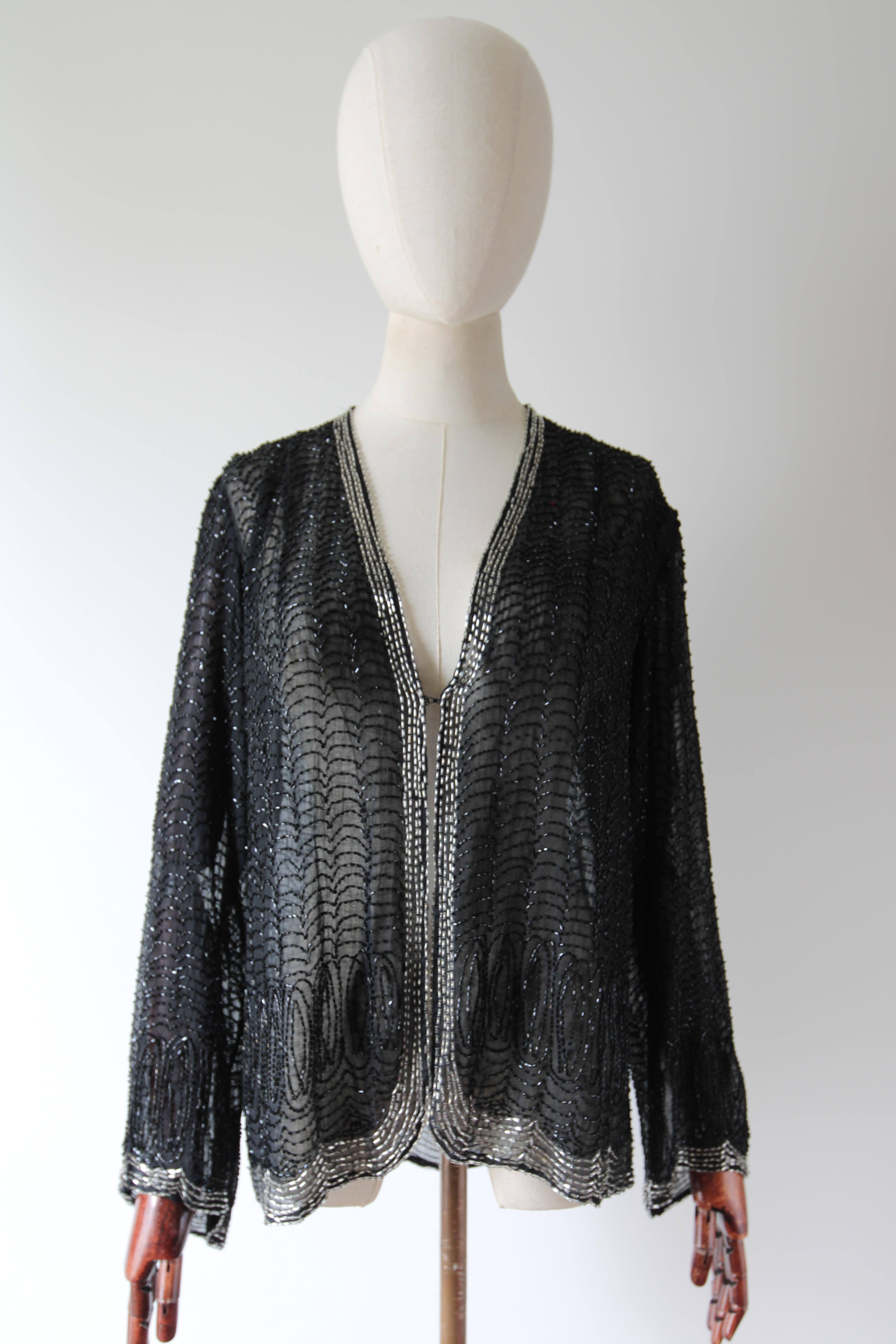 A rare piece to behold. This original 1920's jacket, rendered on a fine cotton voile base, which is in turn embellished with black and silver bugle beads in a scalloped pattern, is the perfect statement piece to your wardrobe. 
The V shaped neckline