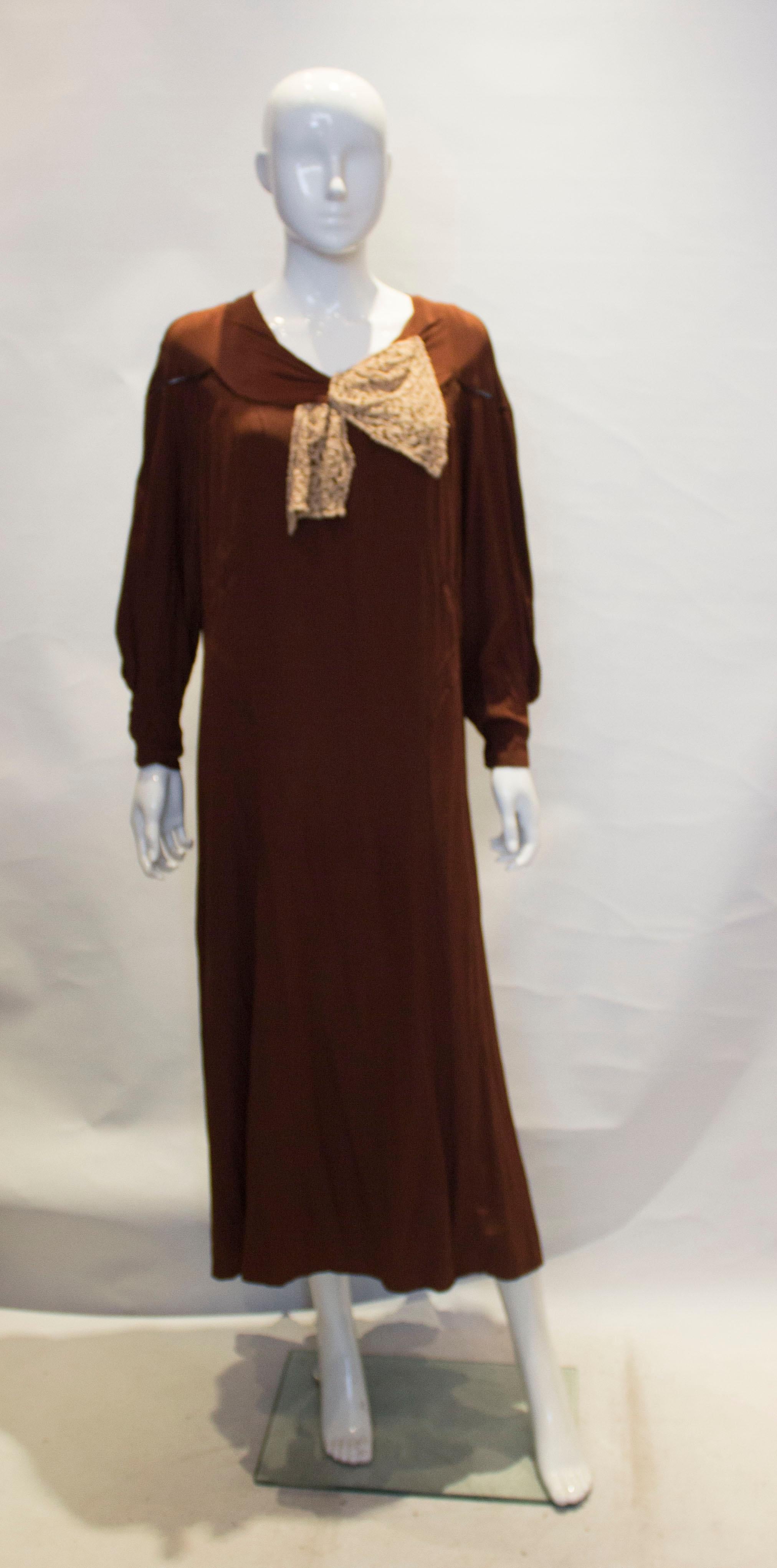 A good brown silk vintage dress from the 1920s. The dress has a round neckline with stitch detail on the front and back., and lace detail on the front. It has popper fastenings at the cuff and is fully lined. It is meant toe be worn loose and will