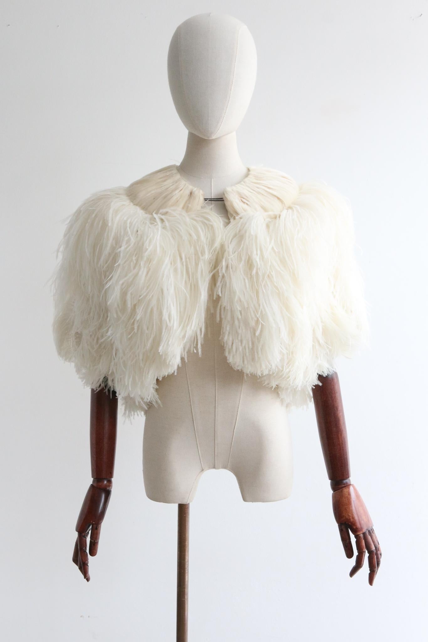 This rare and opulent 1920's cream toned ostrich feather jacket, is a piece to behold.

The rounded neckline is framed by a border of sewn and glued down feathers, creating a soft collar design, that draws together internally along the front of the