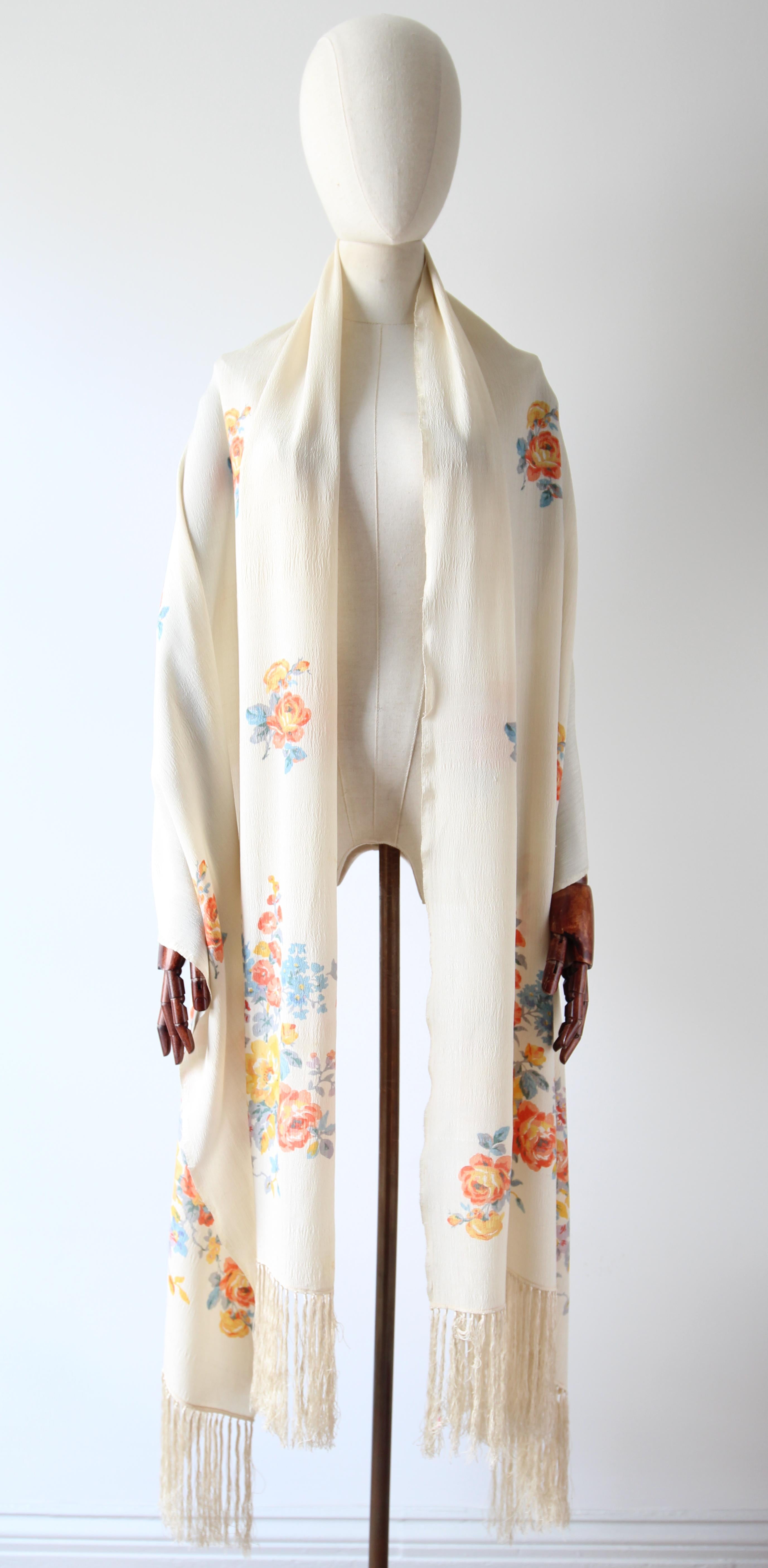 A marvel to behold. This original 1920's cream silk shawl, embellished with a pattern of scattered roses in shades of blush, red, yellow orange and teal greens, framed along each extremity with large trailing wild flower patterns in a matching