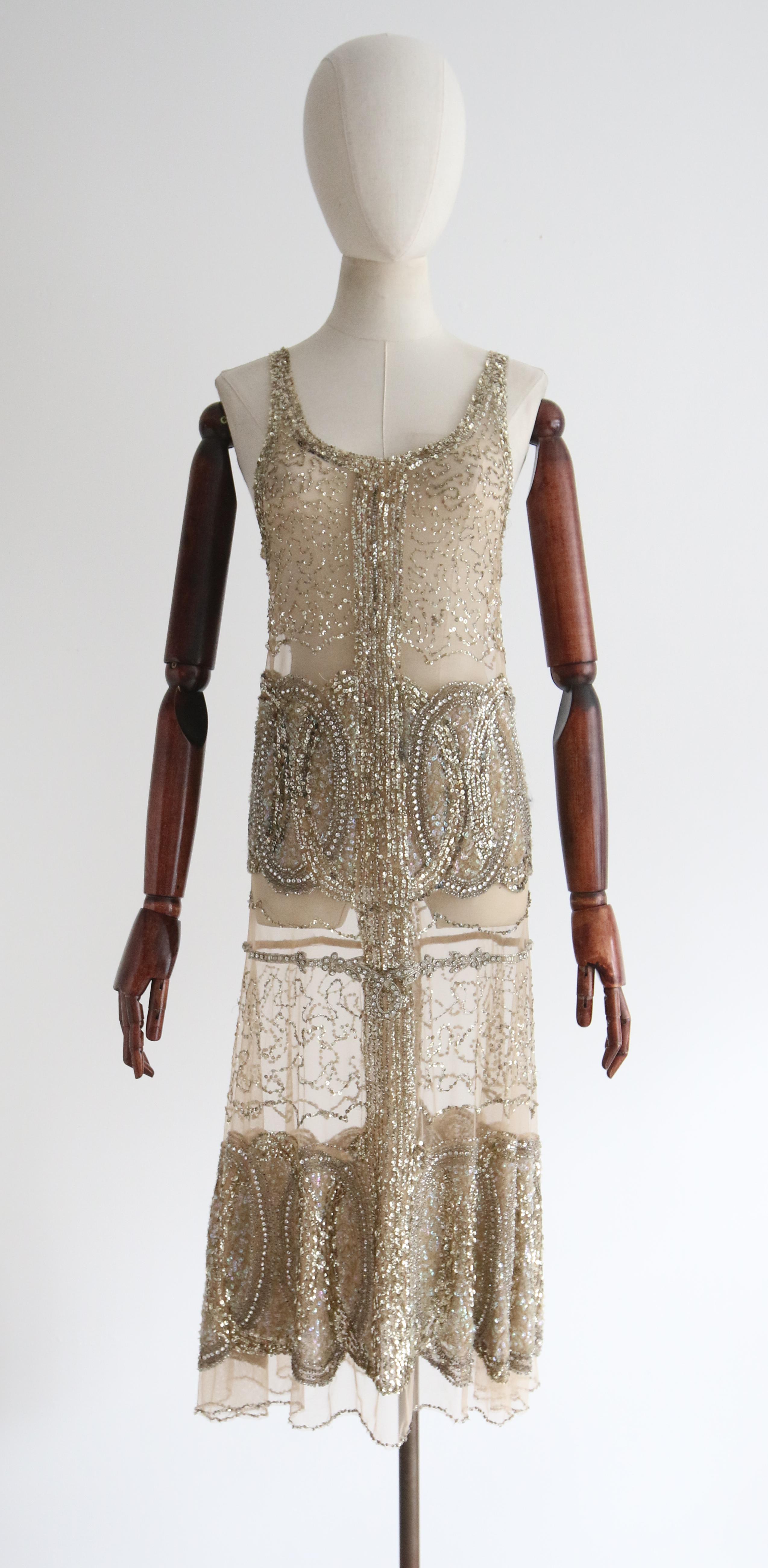 Full of opulent original details, rendered in the most luxurious fashion, this rare 1920's piece is a beauty to behold and never again find.

The rounded neckline of the dress, is framed by a border of gold sequin embellishments, which join a