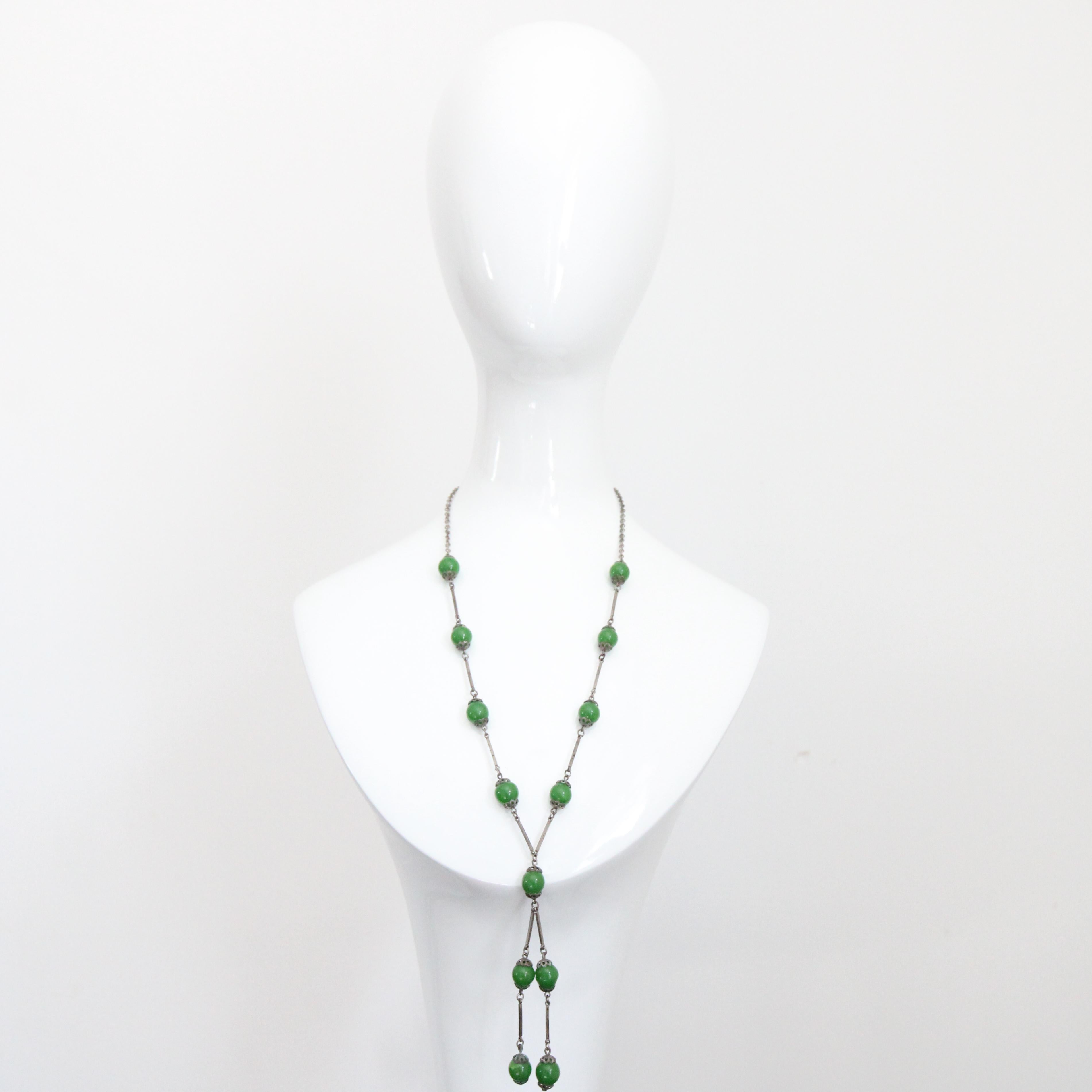 This wonderfully designed 1920's jadeite glass beaded necklace in a vibrant shade of forest green, is a rare piece to behold. On a silver toned metal chain link base, the green glass beads are incased within silver toned metal filigree border beads,