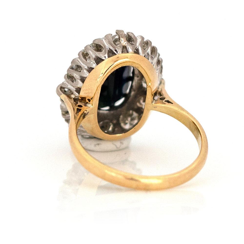 Our vintage 1930s/1940s 18ct yellow and white gold ring was meticulously hand crafted, it features a 5.35ct ink black oval sapphire at its heart, surrounded by a halo of 1.45ct transitional cut diamonds. The ring features transitional cut diamonds