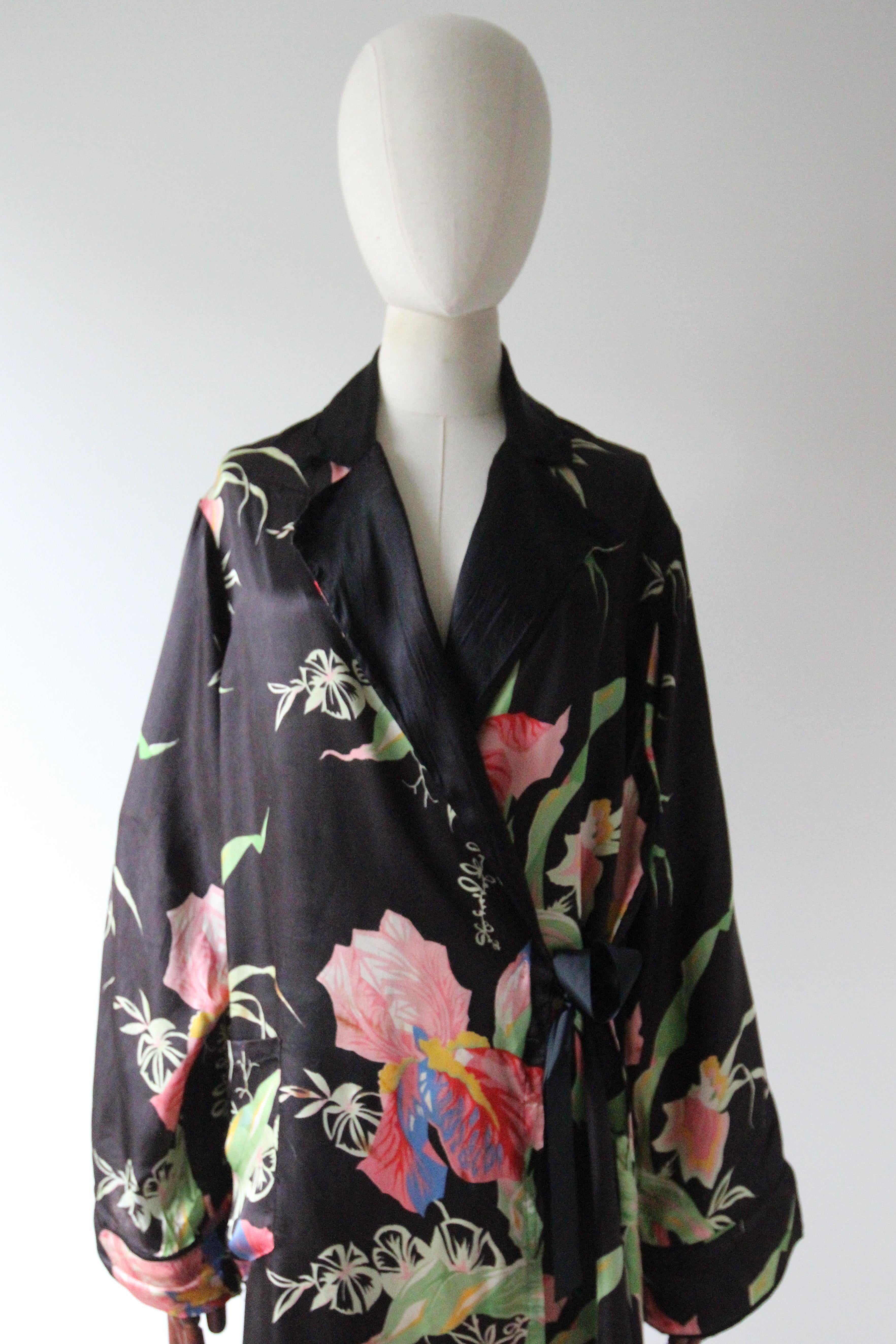 This vintage 1940's black celanese satin robe, with a bright and vibrant pattern of blooming irises in shades of pink, blue, yellow, red and green, is the perfect piece to add to your loungewear collection.

The V shaped neckline is framed by  black
