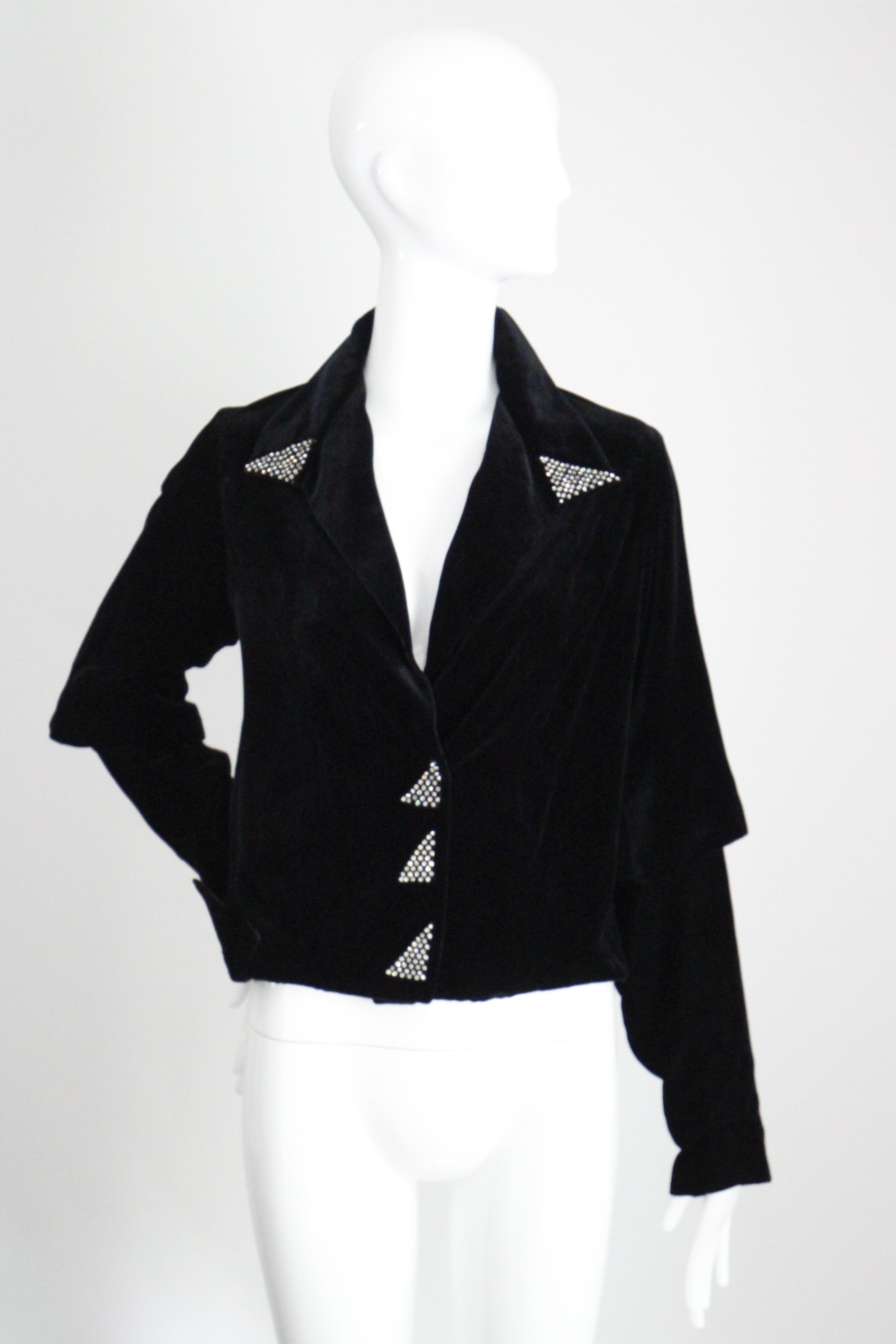 Réalisée dans le plus somptueux velours de soie noir et rehaussée de strass argentés, cette veste originale des années 1930 est la pièce parfaite à ajouter à votre collection vintage.

L'encolure en V est encadrée par un large col pointu, agrémenté