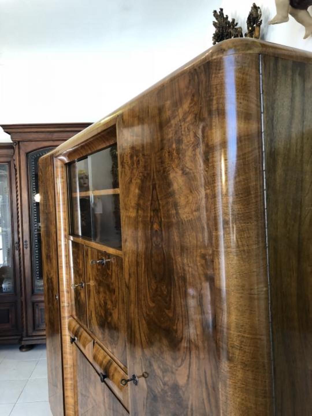 Burl wood Art Deco style cabinet made of Caucasian walnut with a stunning wooden grain. Features plenty of storage space behind multiple doors and a showcase compartment with glass sliding doors on top.
Finished with a high gloss patina finish and