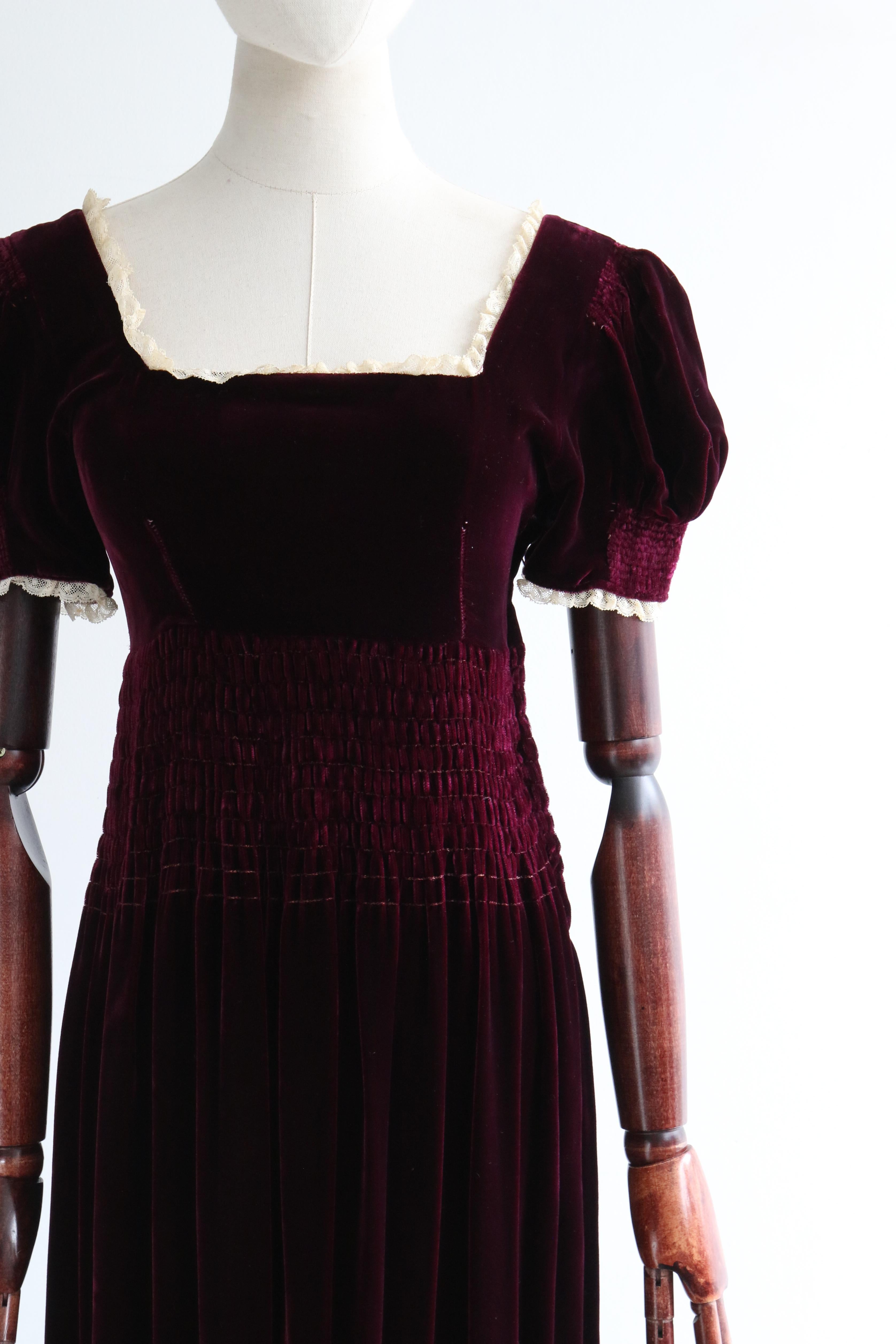 Dieses atemberaubende Kleid aus burgunderrotem Seidensamt aus den 1930er Jahren mit cremefarbenen Spitzendetails ist genau das richtige Stück für Ihre Übergangsgarderobe. 

Der runde Halsausschnitt ist mit einer Borte aus cremefarbener Spitze