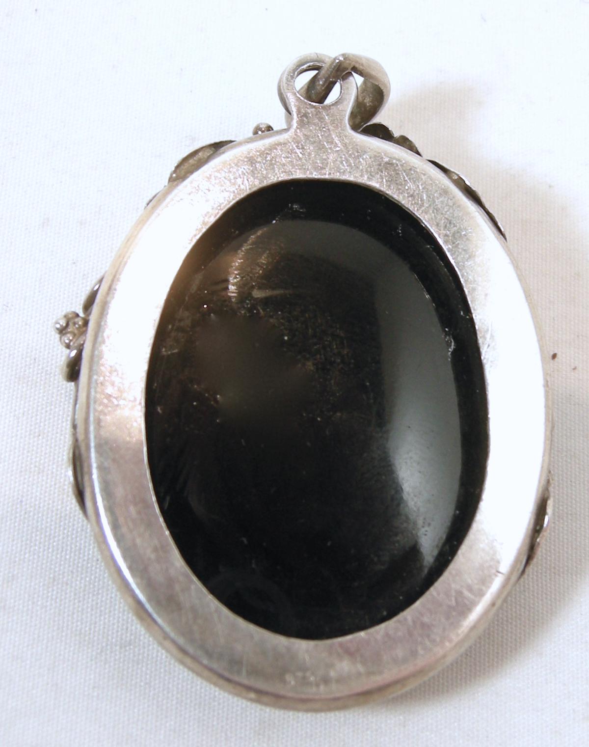 This vintage 1930’s pendant features a large black glass with a butterfly intaglio in a 3-dimensional floral design sterling silver setting.  In excellent condition, this pendant measures 2-1/8” x 1-3/8”.
