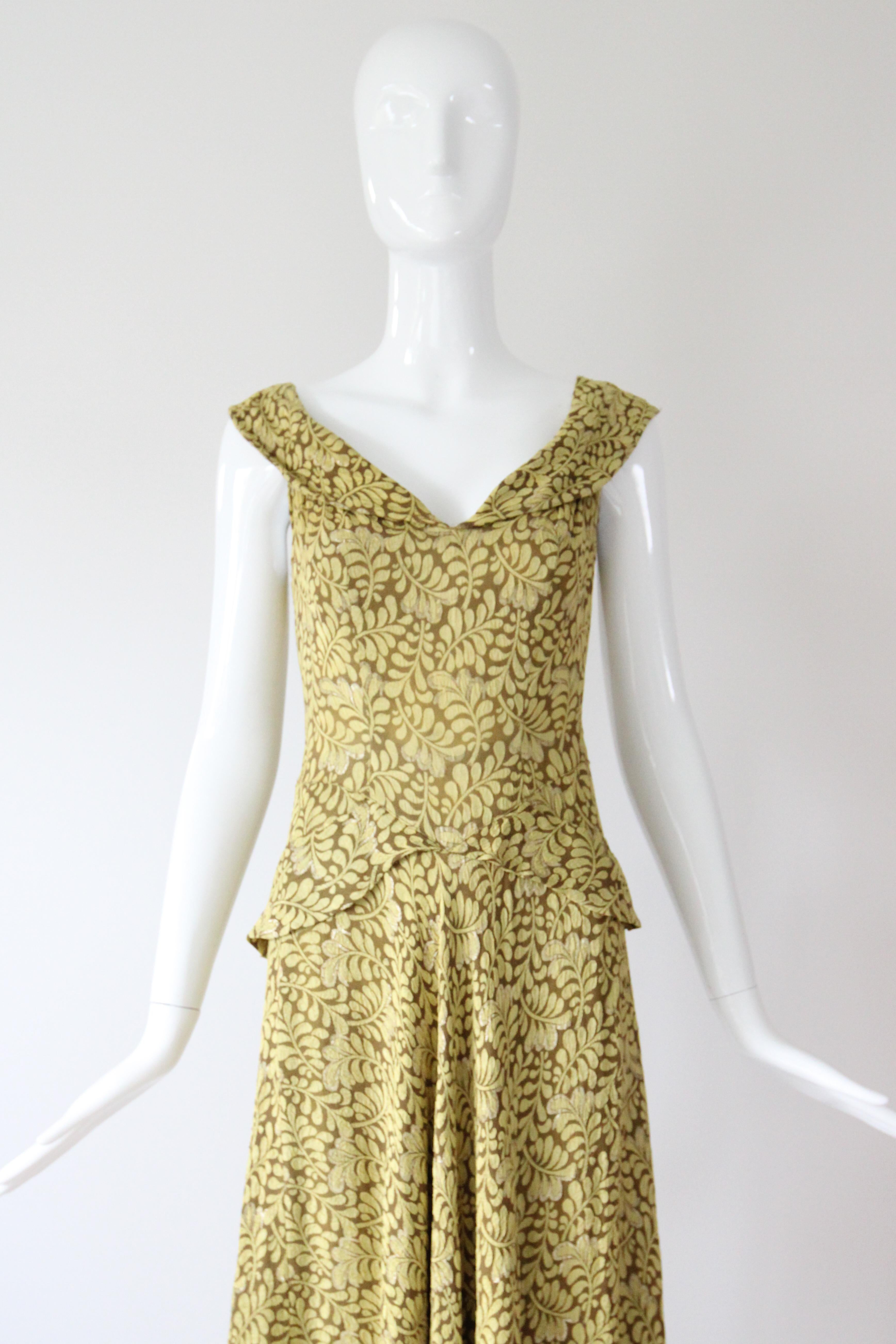 Dieses bezaubernde Kleid mit botanischem Druck in Chartreusegrün und Braun aus den 1930er Jahren mit Akzenten aus goldenen Laméfäden ist eine Rarität.

Ihr runder Ausschnitt wird von einem weichen Umlegekragen eingerahmt, der die Schultern in