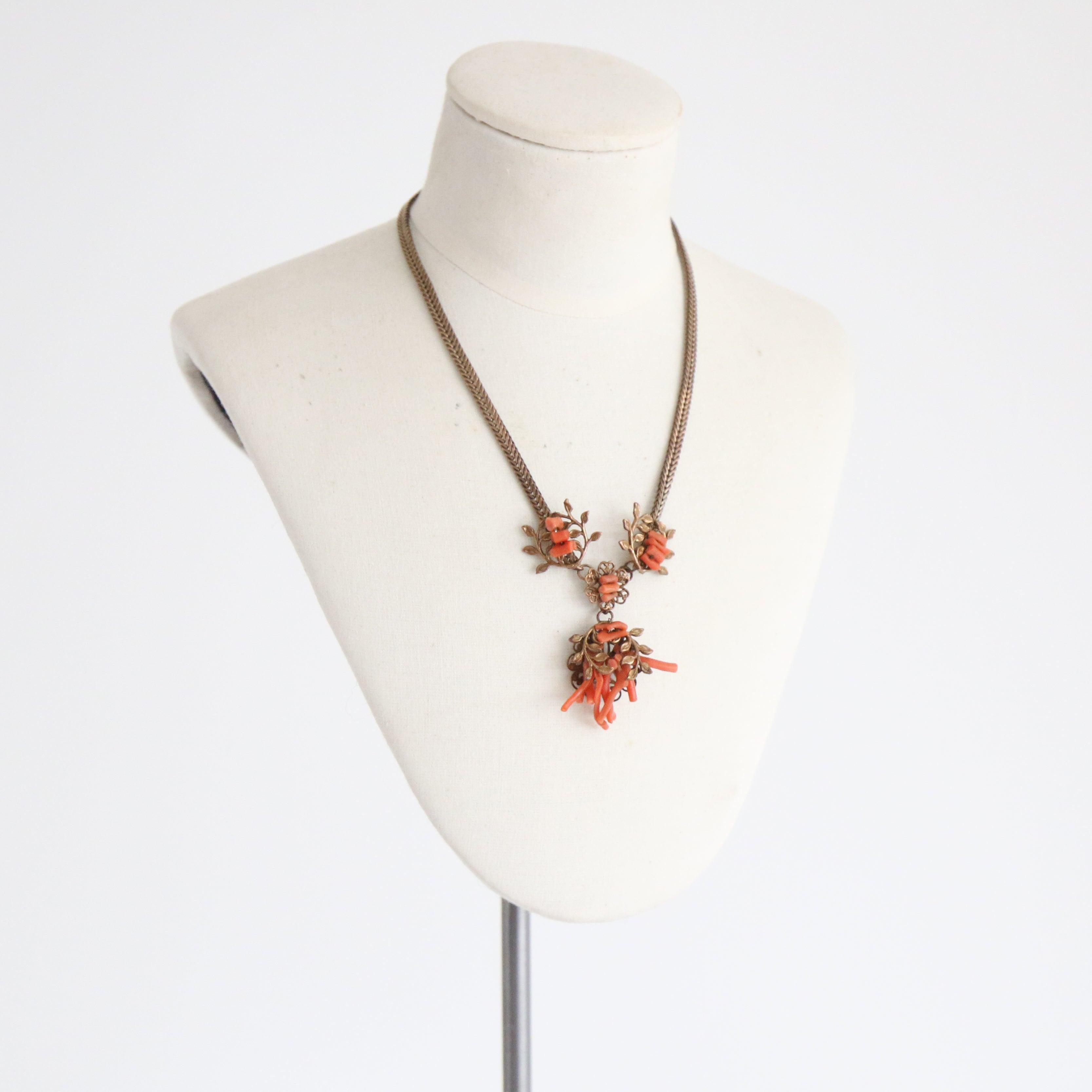 Cet époustouflant collier des années 1930, monté sur une chaîne serpent en laiton, est décoré au centre de quatre pendentifs en filigrane botanique avec des éléments en corail câblé. Terminé par un fermoir-boîte à poussoir assorti, chaque détail de