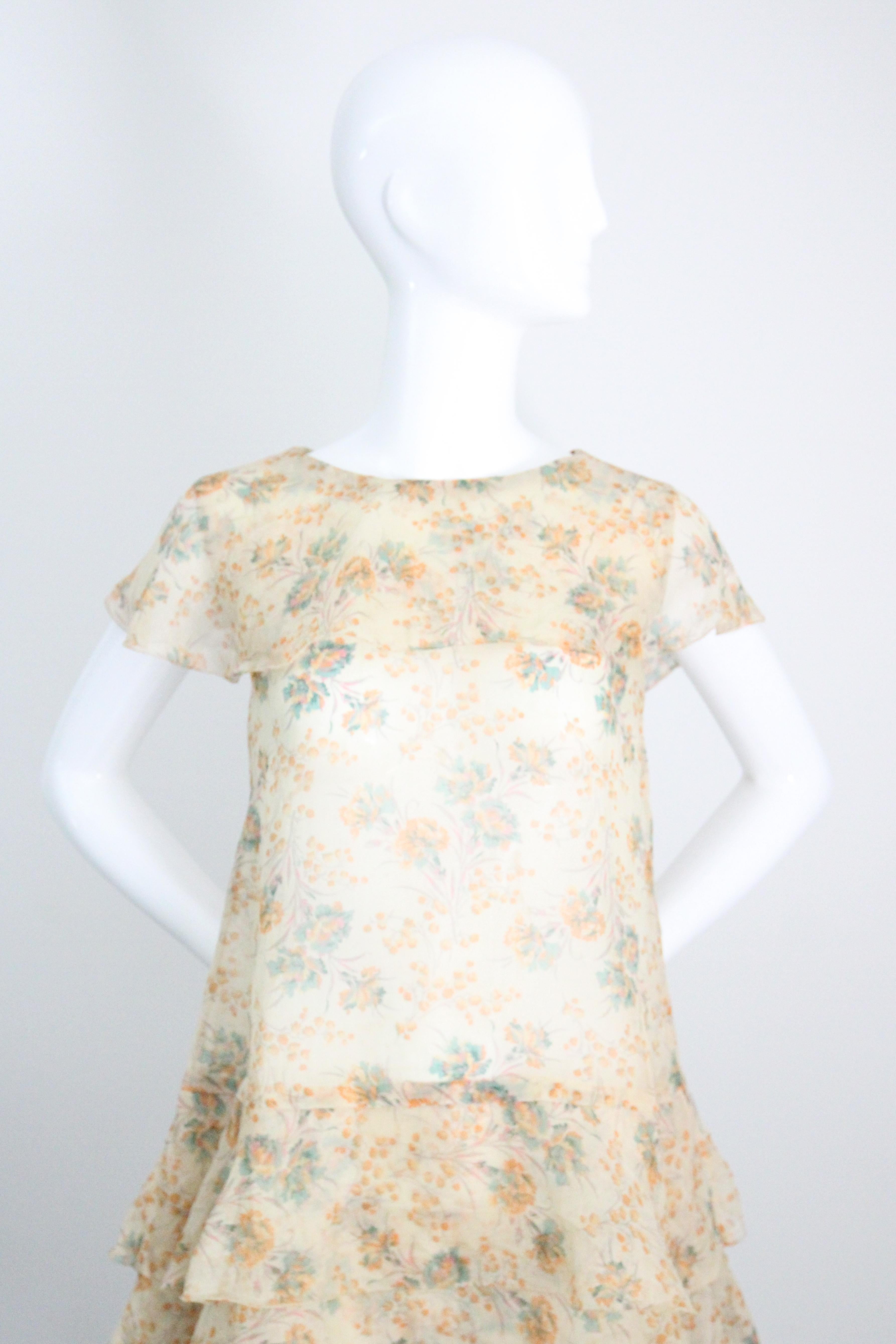 Este original vestido de día de gasa de algodón crema de los años 30, con un encantador estampado de claveles y flores silvestres, en tonos apagados de verde, naranja, amarillo y rosa rubor, es la prenda perfecta para dar la bienvenida al buen