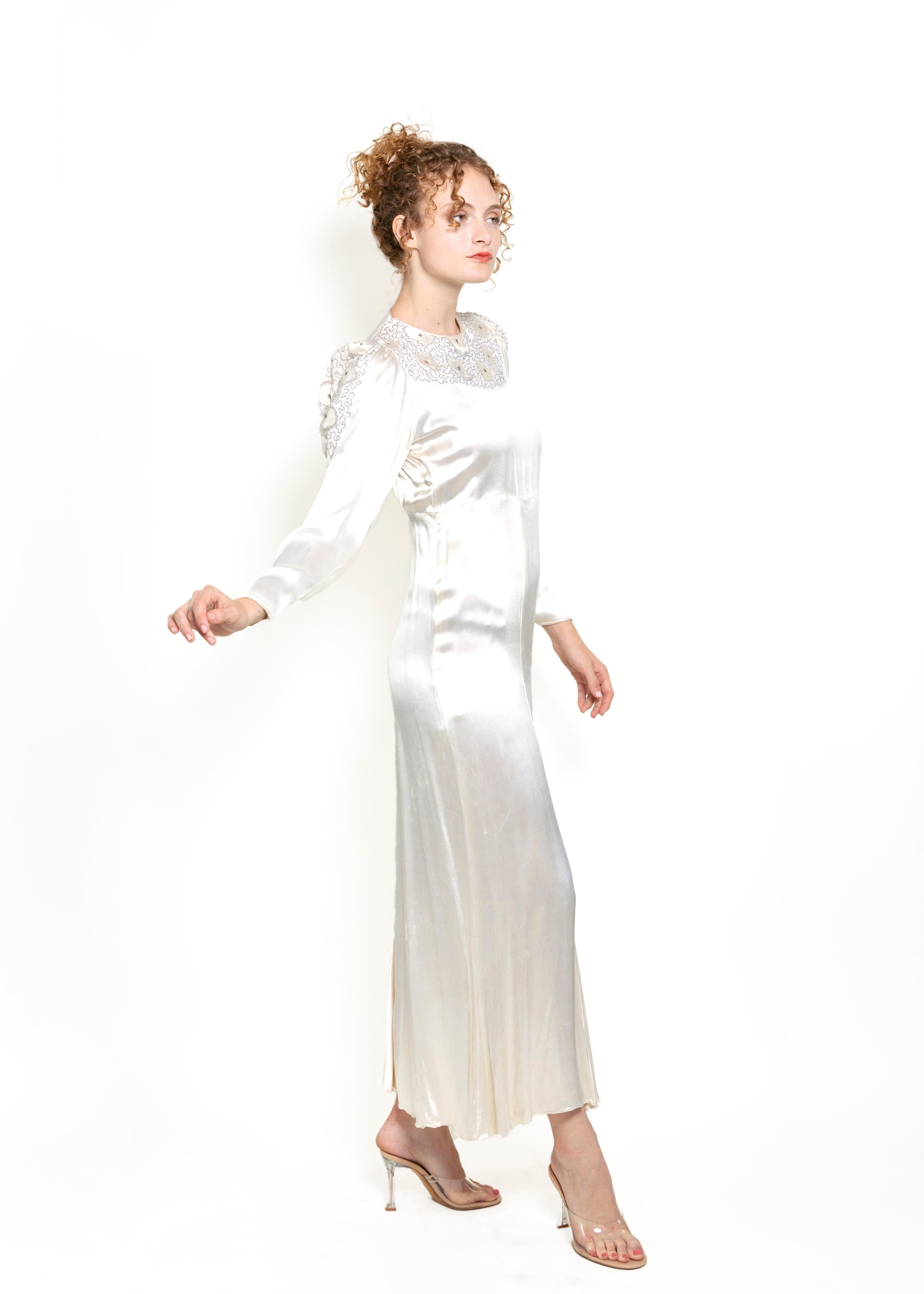 This Vintage 1930s Cream Silk Embroidered Gown is a timeless and elegant piece of wearable art. Its luxurious satin silk construction adorned with intricate embroidered detail and snap cuff sleeves creates an exclusive and sophisticated look. It's