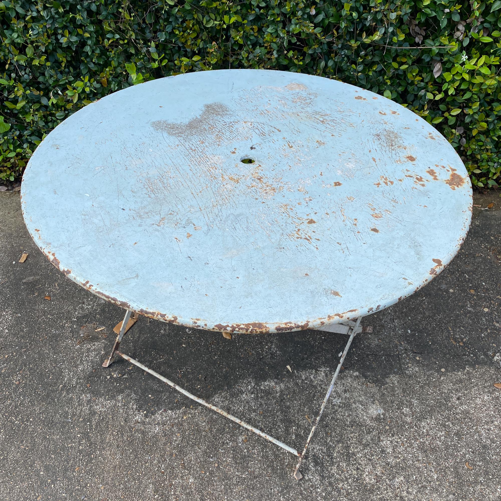 A charming and functional round metal folding table that can be used almost anywhere, this 1930s French metal table features a very pale sky blue finish and space for an umbrella. The simple wrought iron legs are painted to match and the table opens