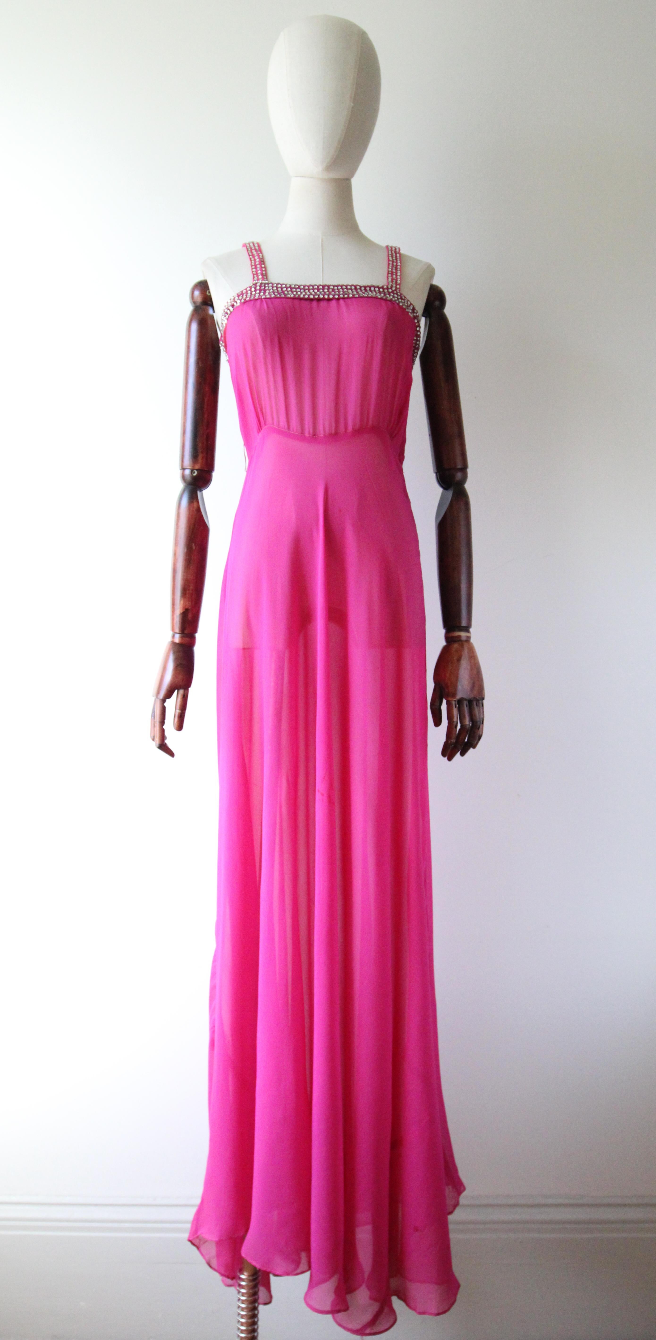 Este original vestido de los años 30 y su capelina a juego, en el tono más vibrante de la gasa de seda rosa fucsia y adornados con brillantes plateados, es la pieza perfecta para tu colección vintage.

 El corte cuadrado del escote está enmarcado