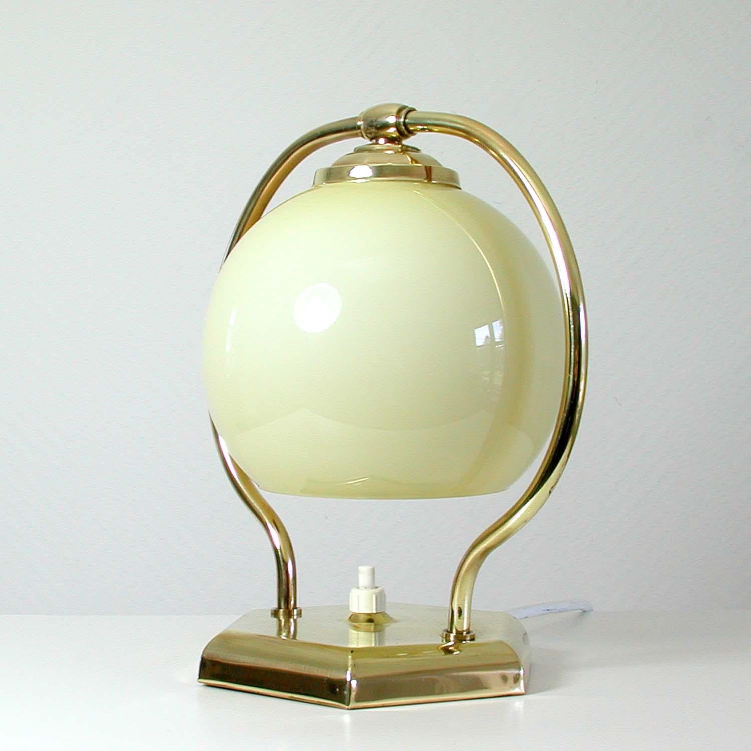 This vintage table or bedside lamp was made in Germany in the 1930s during the Bauhaus period. It is made of polished brass and has got an adjustable lamp shade in opaline glass.