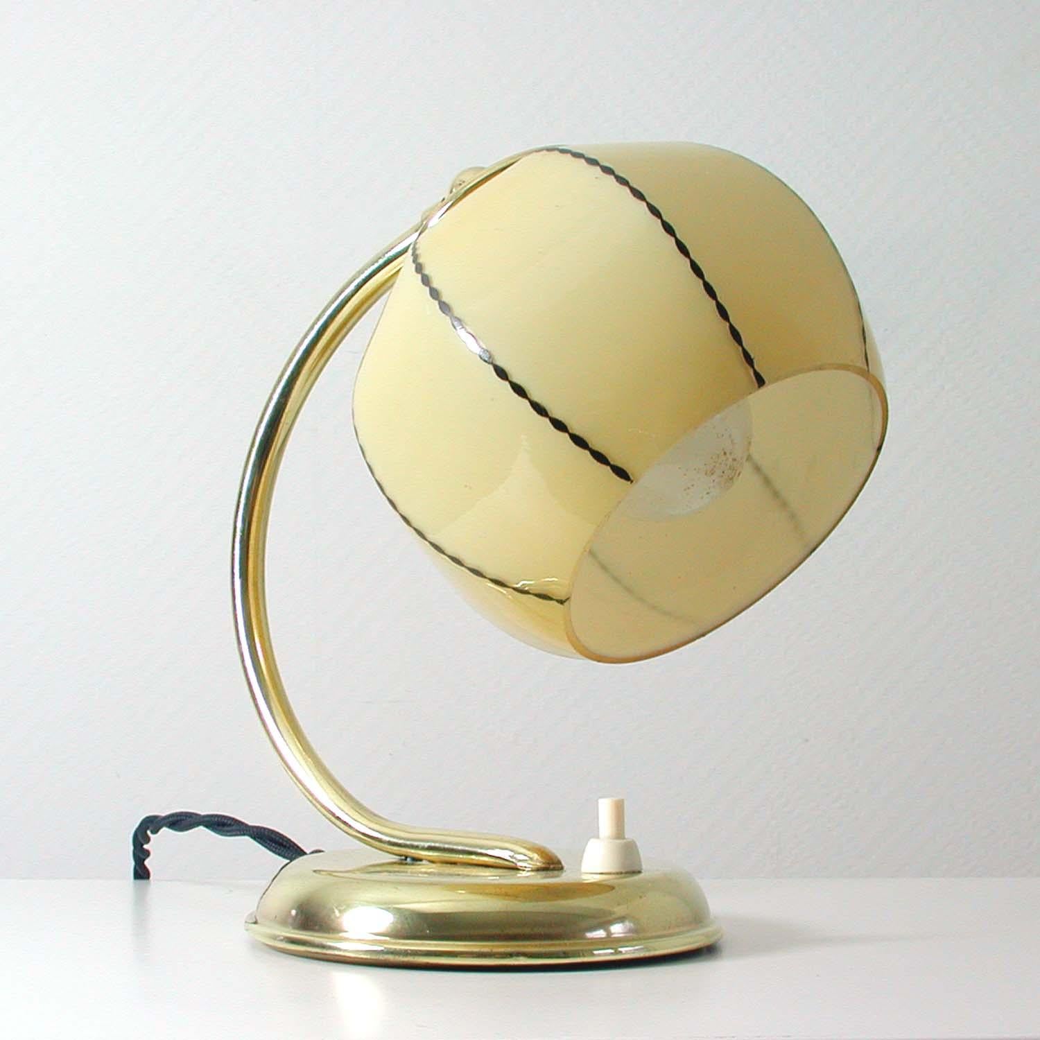 This vintage table or bedside lamp was made in Germany in the 1930s during the Bauhaus period. It is made of polished brass and has got an adjustable lamp shade in opaline glass. The glass shade is cream with black details.
The lamp can be used as