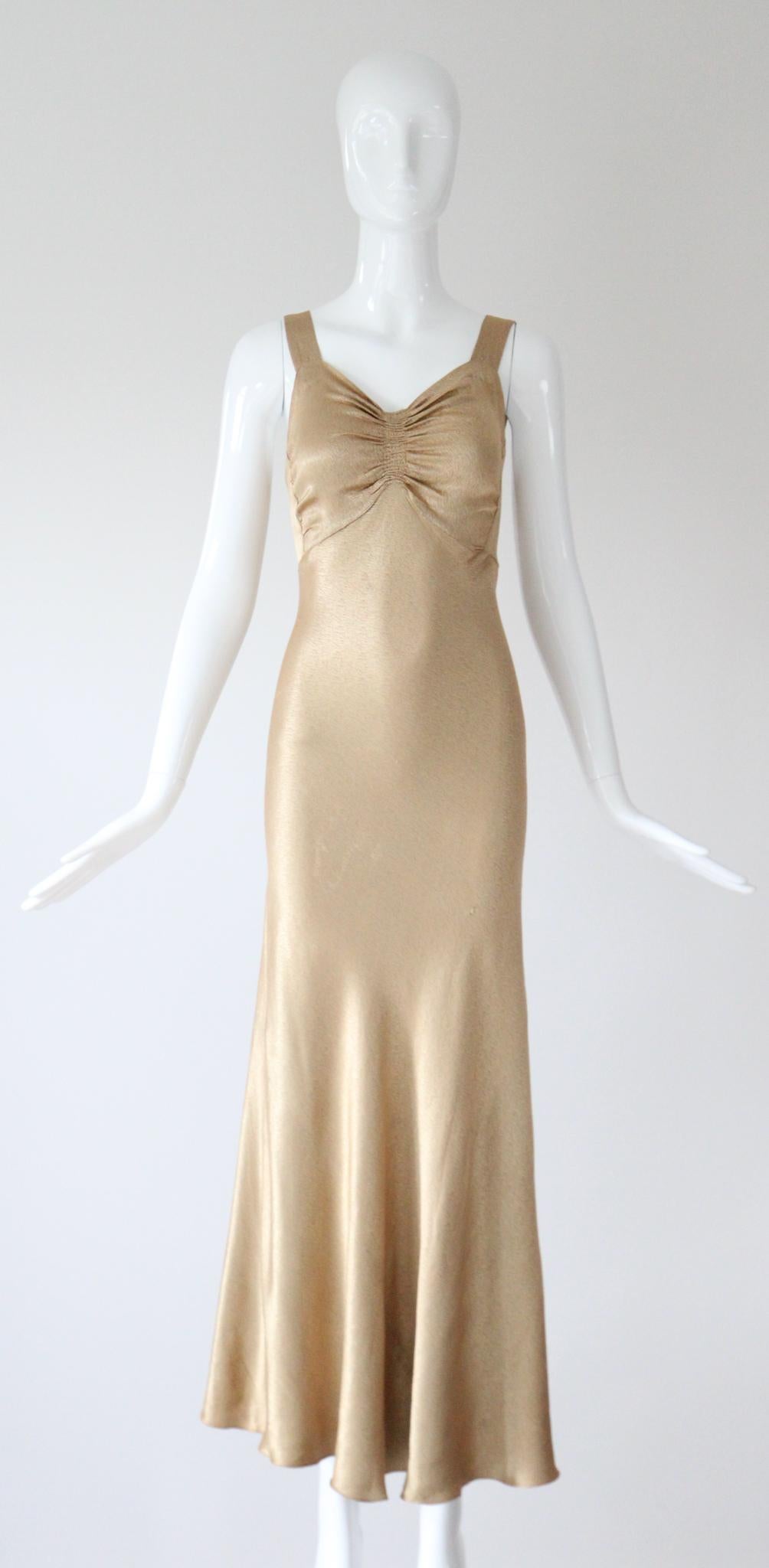 Dieses originale Kleid aus den 1930er Jahren und die dazu passende Jacke sind aus prächtigem goldenem Seidensatin gefertigt und ein seltenes Set, das man nie wieder finden wird. 

Der herzförmige Ausschnitt des Kleides wird von breiten