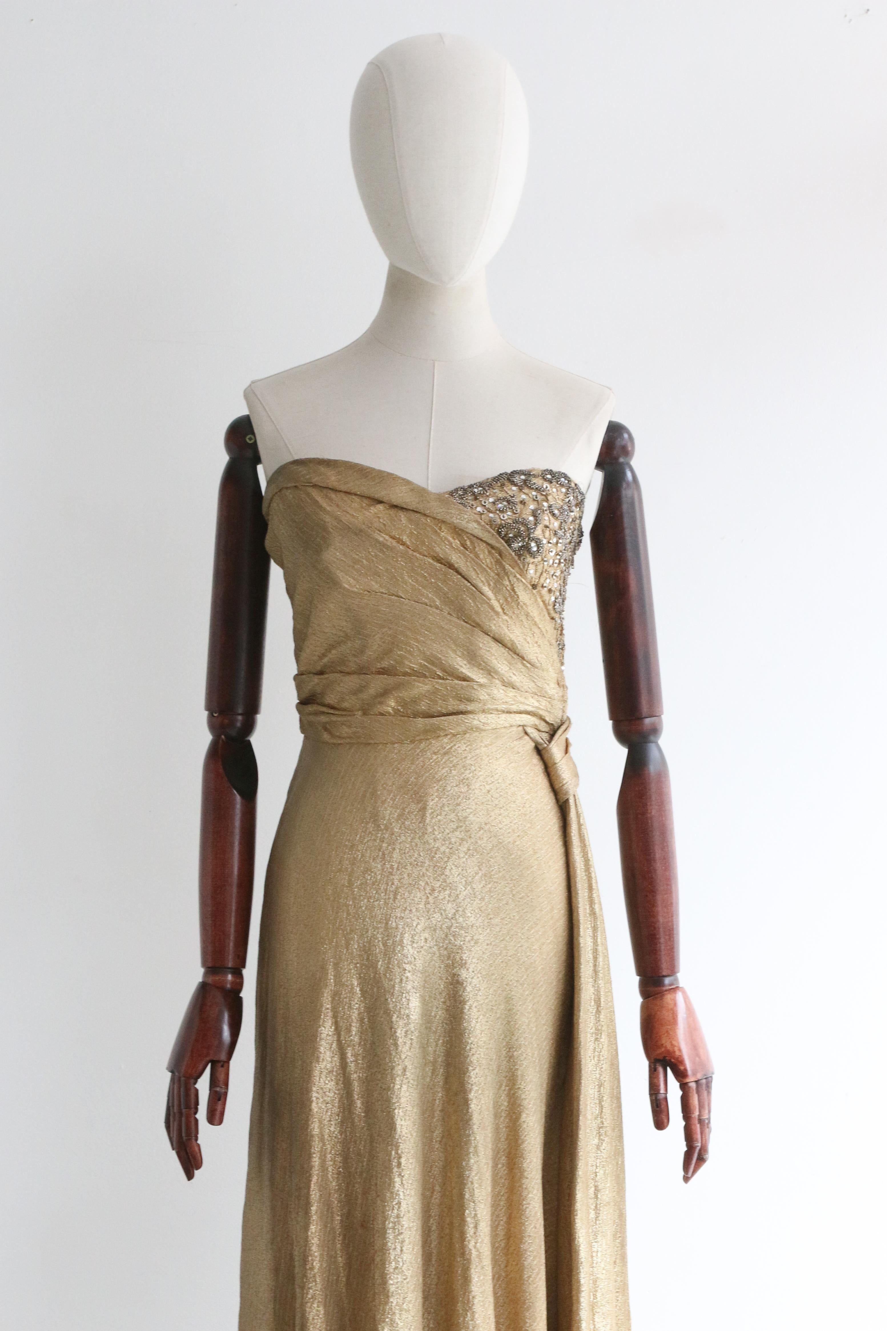 Dieses wahrhaft prächtige Kleid aus goldenem Seidenlamé aus den 1930er Jahren, das mit grauen und silbernen Perlen verziert ist, ist ein phänomenales Stück für Ihre Abendgarderobe.

Das trägerlose Dekolleté des Kleides wird von einem taillierten und