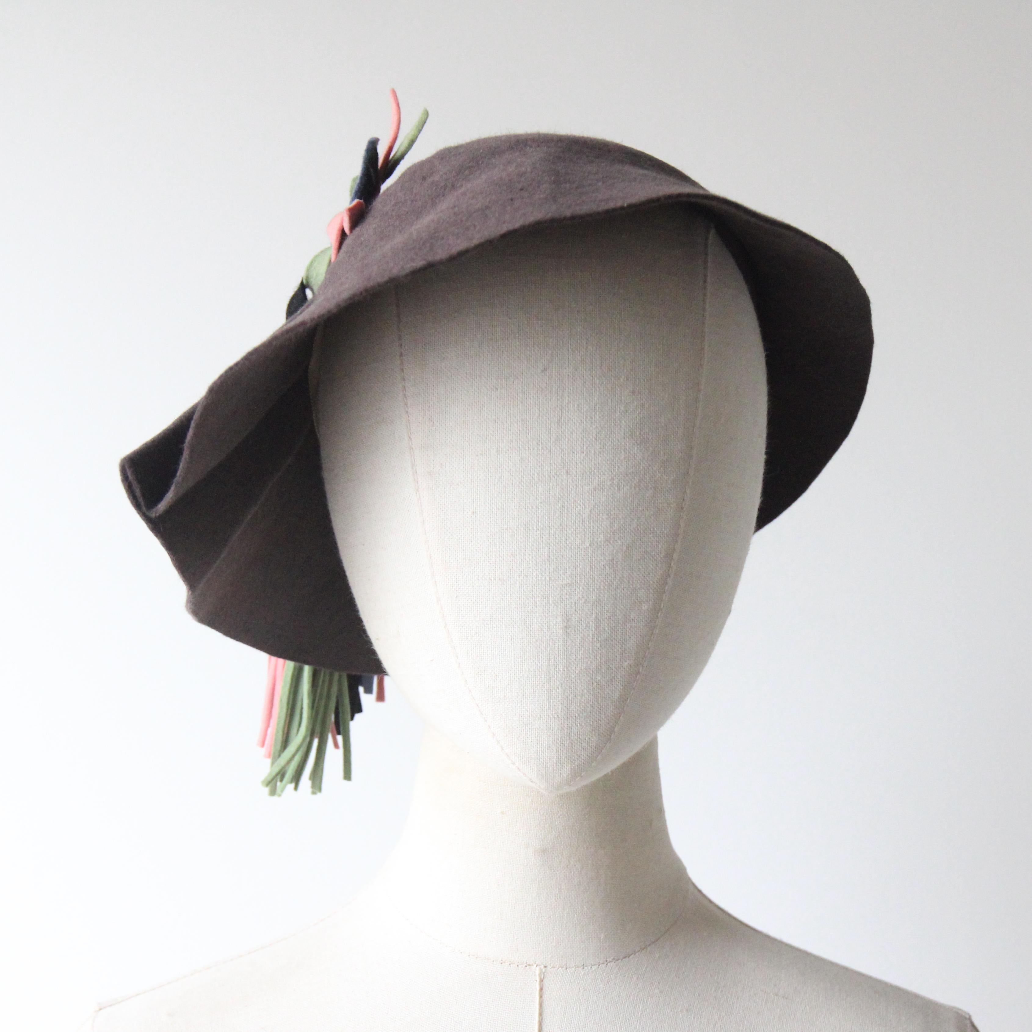 Questo magnifico cappello in pelliccia e feltro di lana degli anni '30, realizzato in un profondo grigio ardesia e arricchito da dettagli in feltro color pastello, è il tocco finale perfetto per il tuo guardaroba stagionale. 

La semplice corona