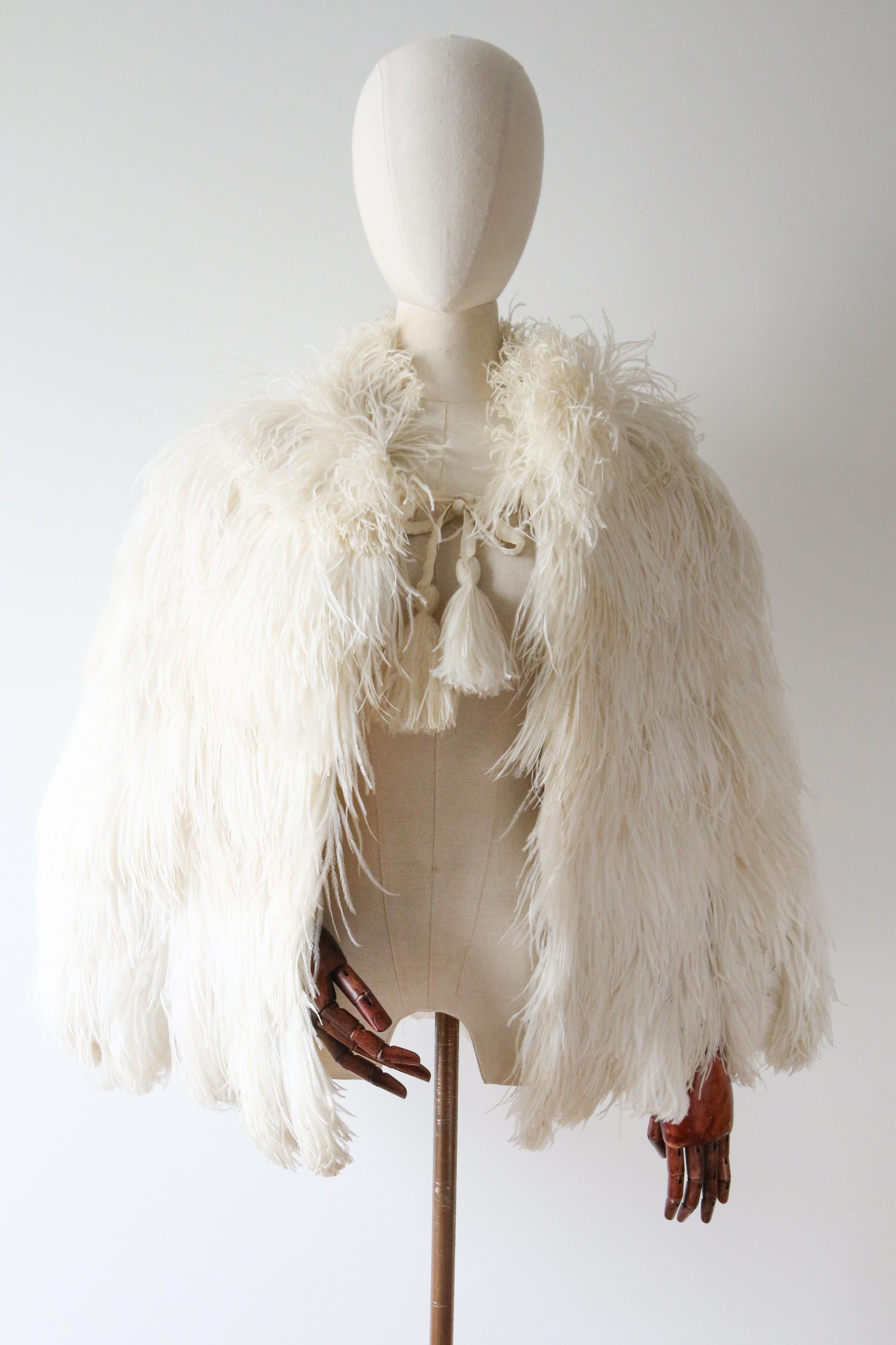This rare and opulent 1930's ivory coloured ostrich feather cape, is a piece to behold.

The amazing plumage of ivory toned ostrich feathers, envelope the neckline and shoulders in a plush plumage . Drawn together to the front, with soft matching