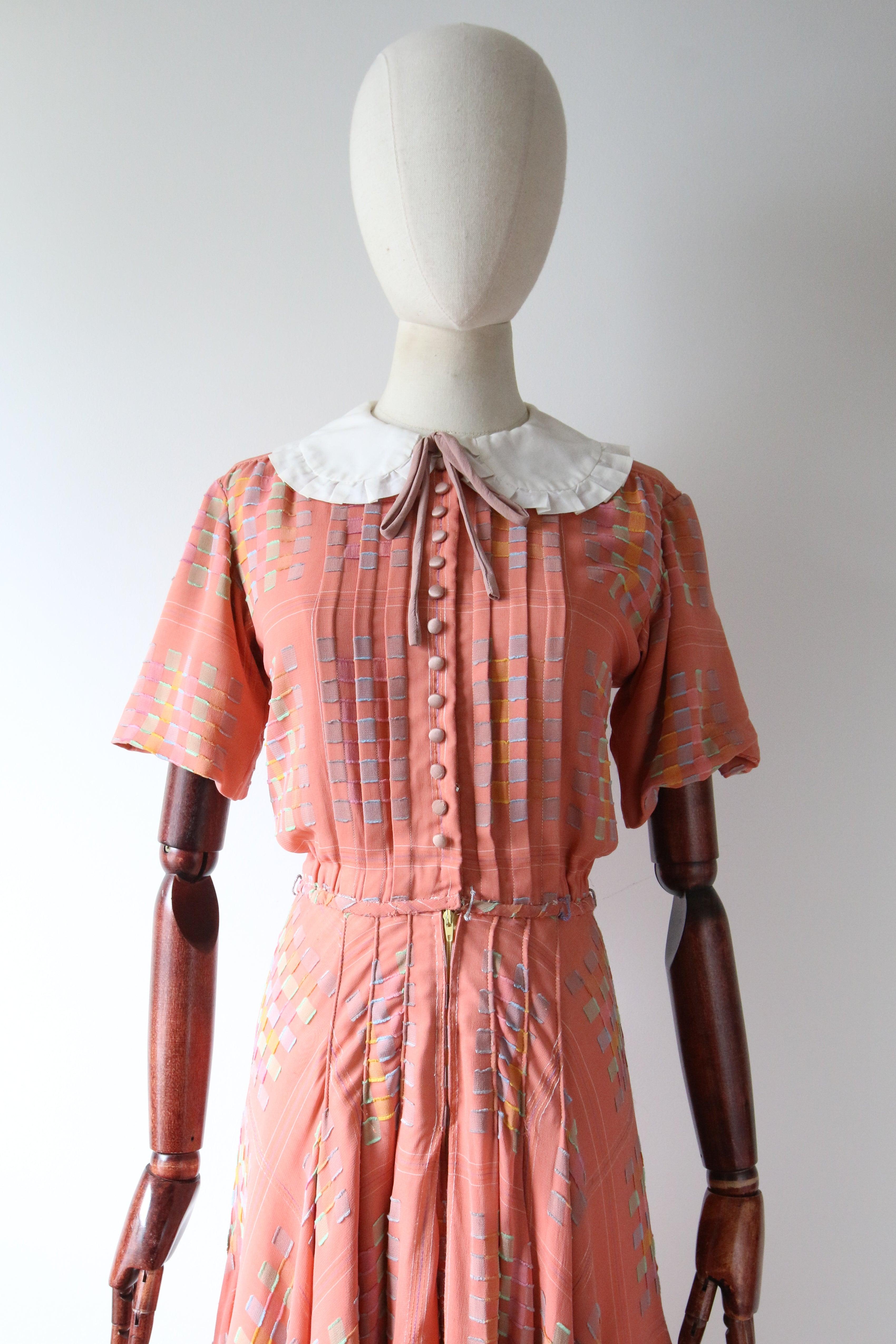 This darling vintage 1930's pink silk dress, with a woven pattern in shades of pastel blue, yellow, green, and pink, accented by soft threaded edges, is the perfect piece to add to your vintage collection. 

The rounded neckline of the dress is