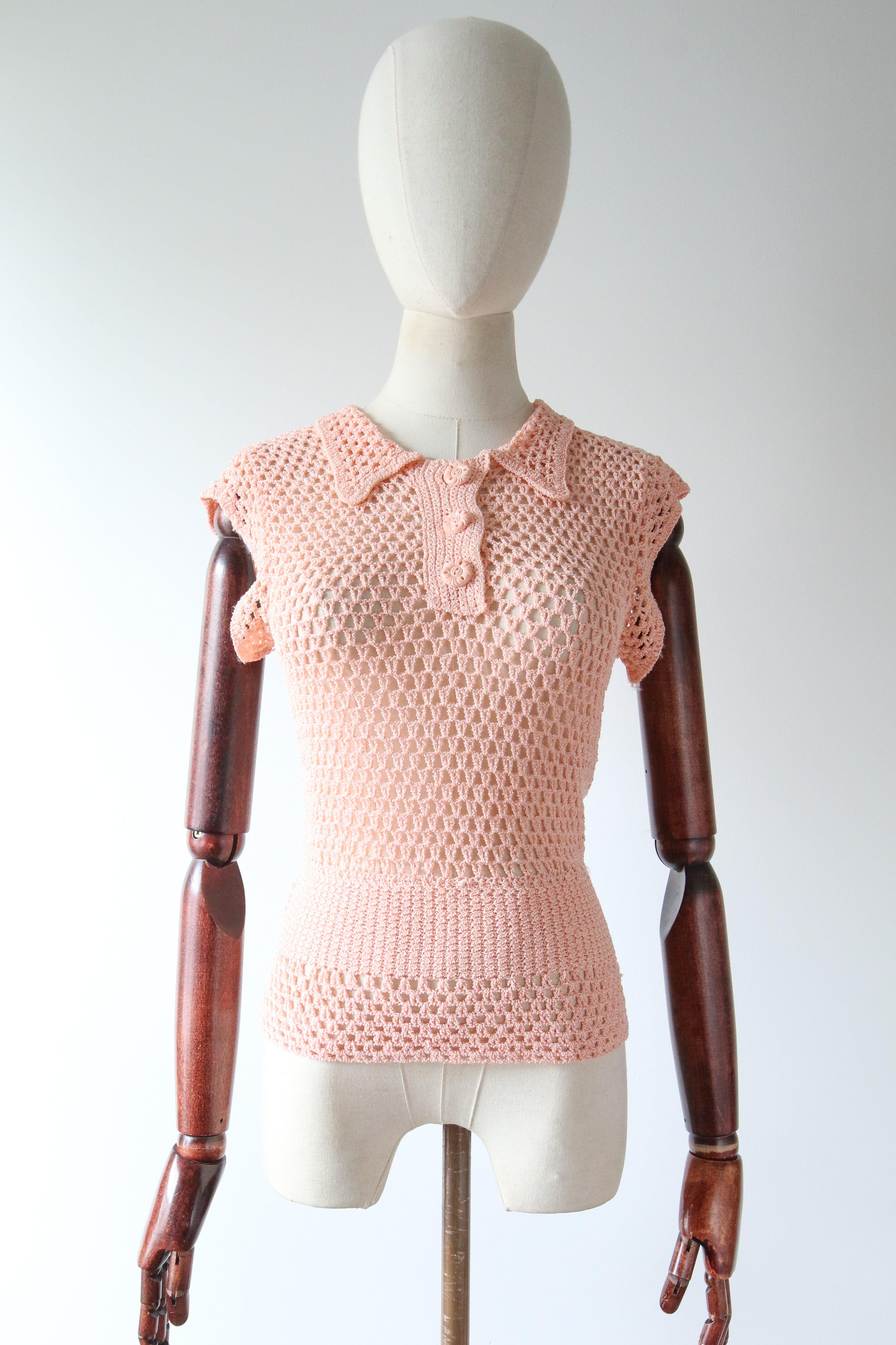 Questa meravigliosa e rara blusa all'uncinetto degli anni '30, realizzata in una fibra di tipo rayon in una vibrante tonalità di rosa, è proprio il capo da abbinare tutto l'anno.

La scollatura arrotondata è incorniciata da un morbido colletto a