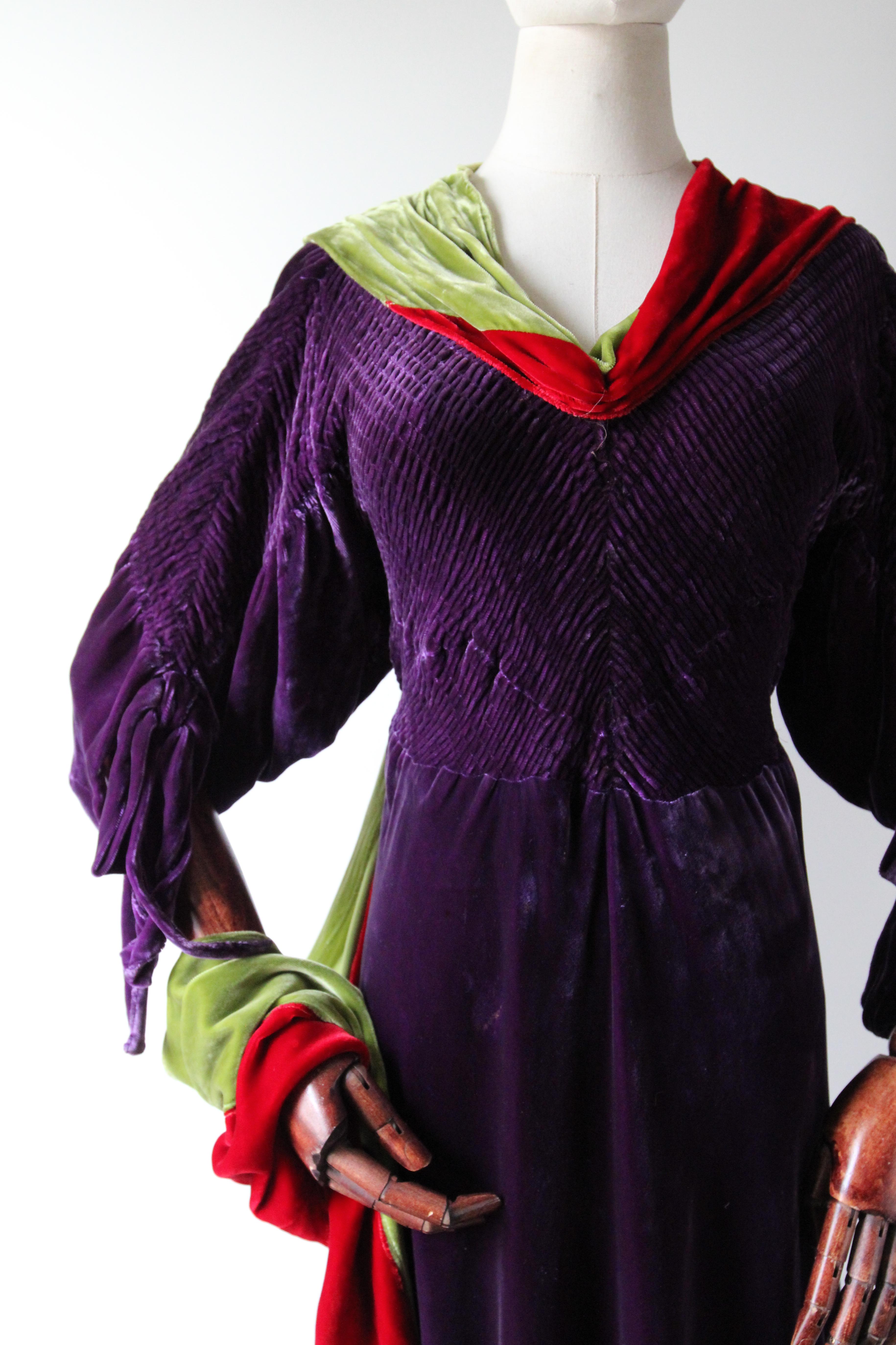Este encantador vestido de terciopelo de seda de los años 30, en un trío de colores: morado real, acentuado con rojo baya y verde lima, es la pieza perfecta para añadir a tu colección vintage. 

El escote en V del vestido está enmarcado por un
